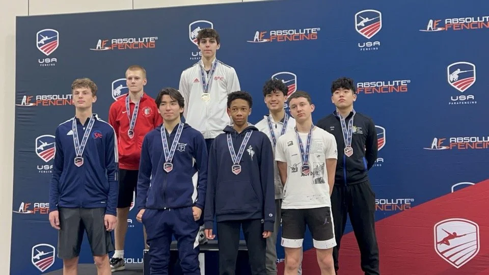 Group of eight young male athletes on a winners' podium at an fencing competition, wearing medals. The backdrop displays 'Absolute Fencing USA'.