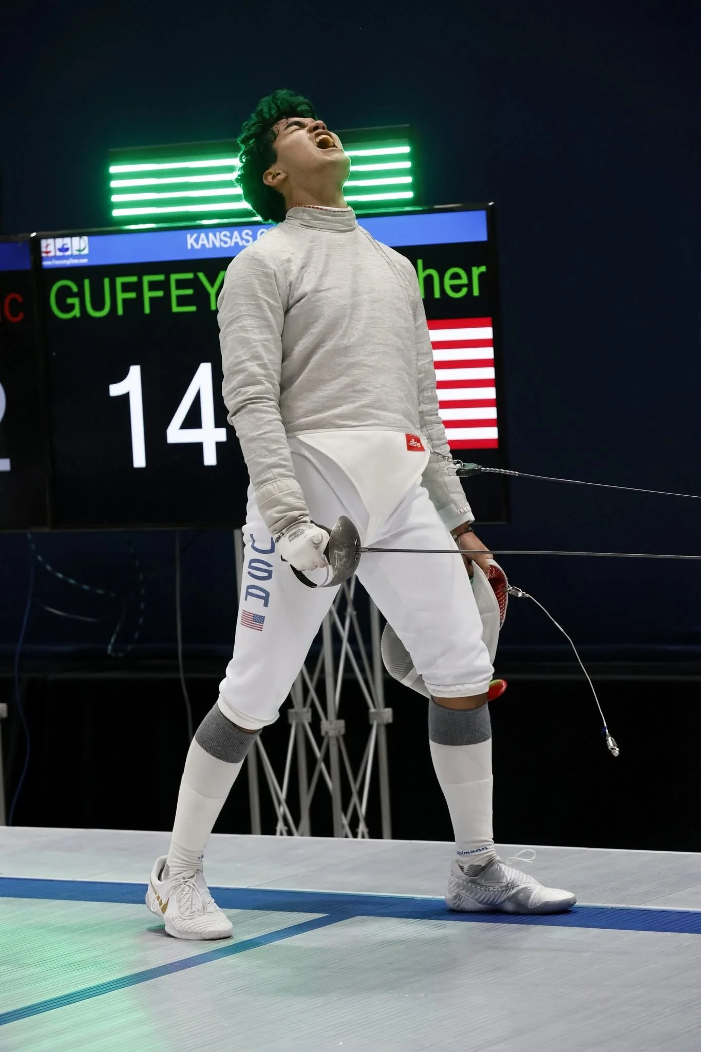 Fencer from the United States on a podium celebrating after a match, with a scoreboard in the background displaying his name Guffey and score 14.