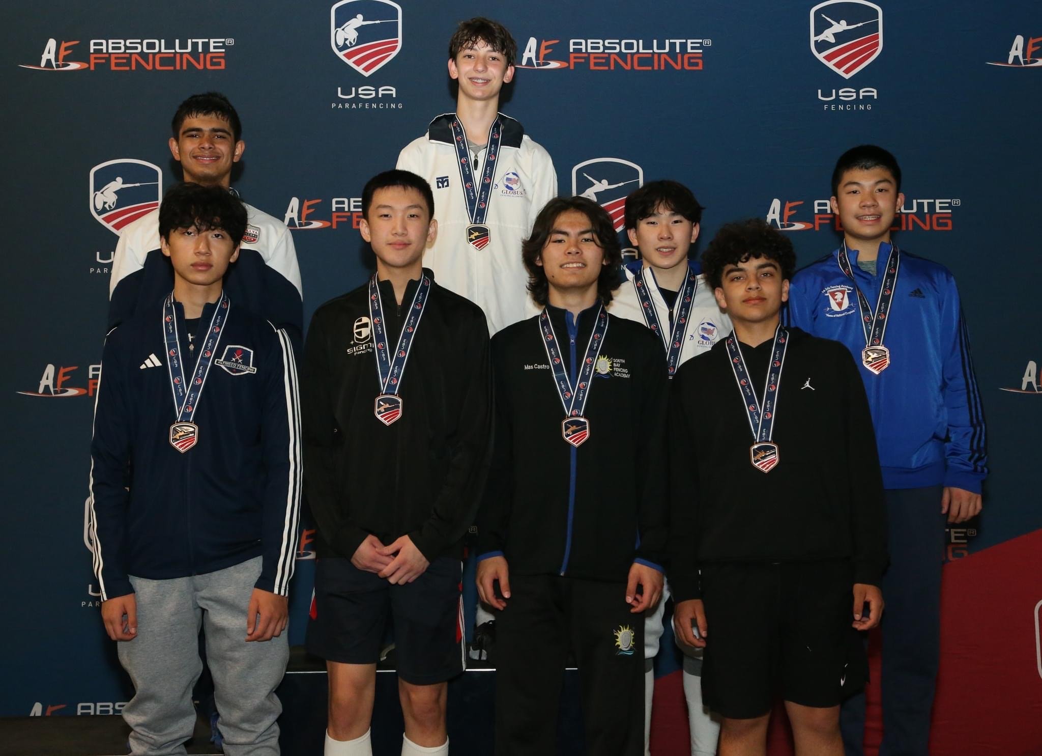 Group of nine young male fencers standing with medals at a fencing competition, backdrop displays logos for Absolute Fencing and USA Fencing.
