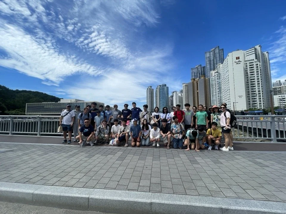 Group of people posing on a bridge with city skyscrapers in the background on a sunny day.
