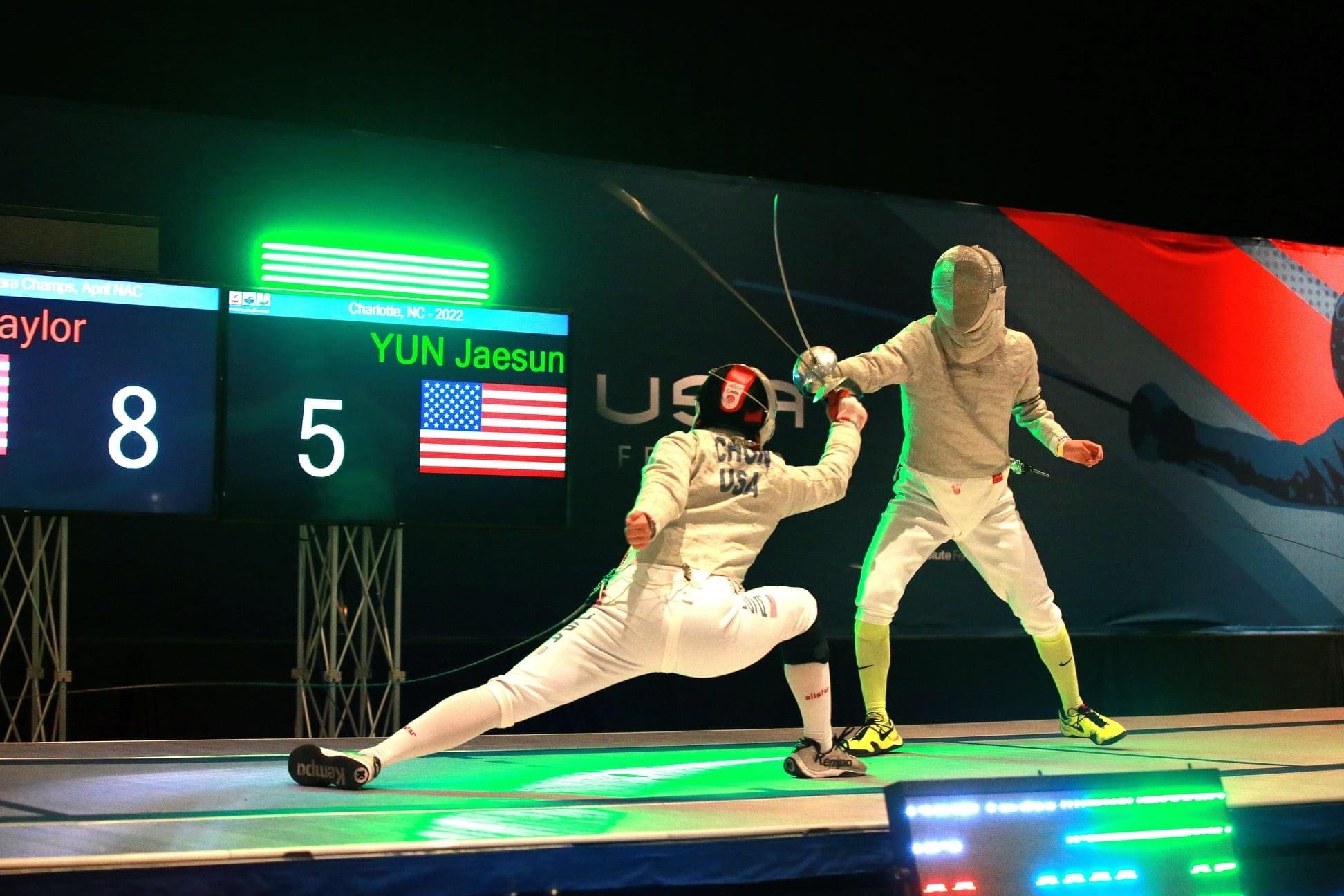 Two American fencers in white uniforms and masks fencing on a green-lit stage with a scoreboard showing 8 to 5 in favor of the opposing team, with a large US flag and the text 'YUN Jaesun' in the background.