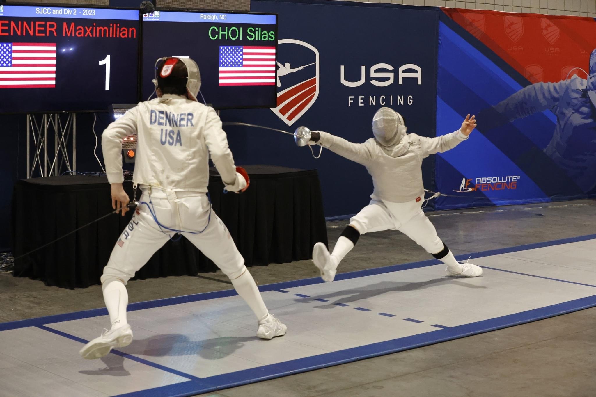 Two fencers in white gear competing in a match on a fencing strip, with LED scoreboard in the background displaying names 'Maximilian Denner' and 'Choi Silas' and USA fencing branding.