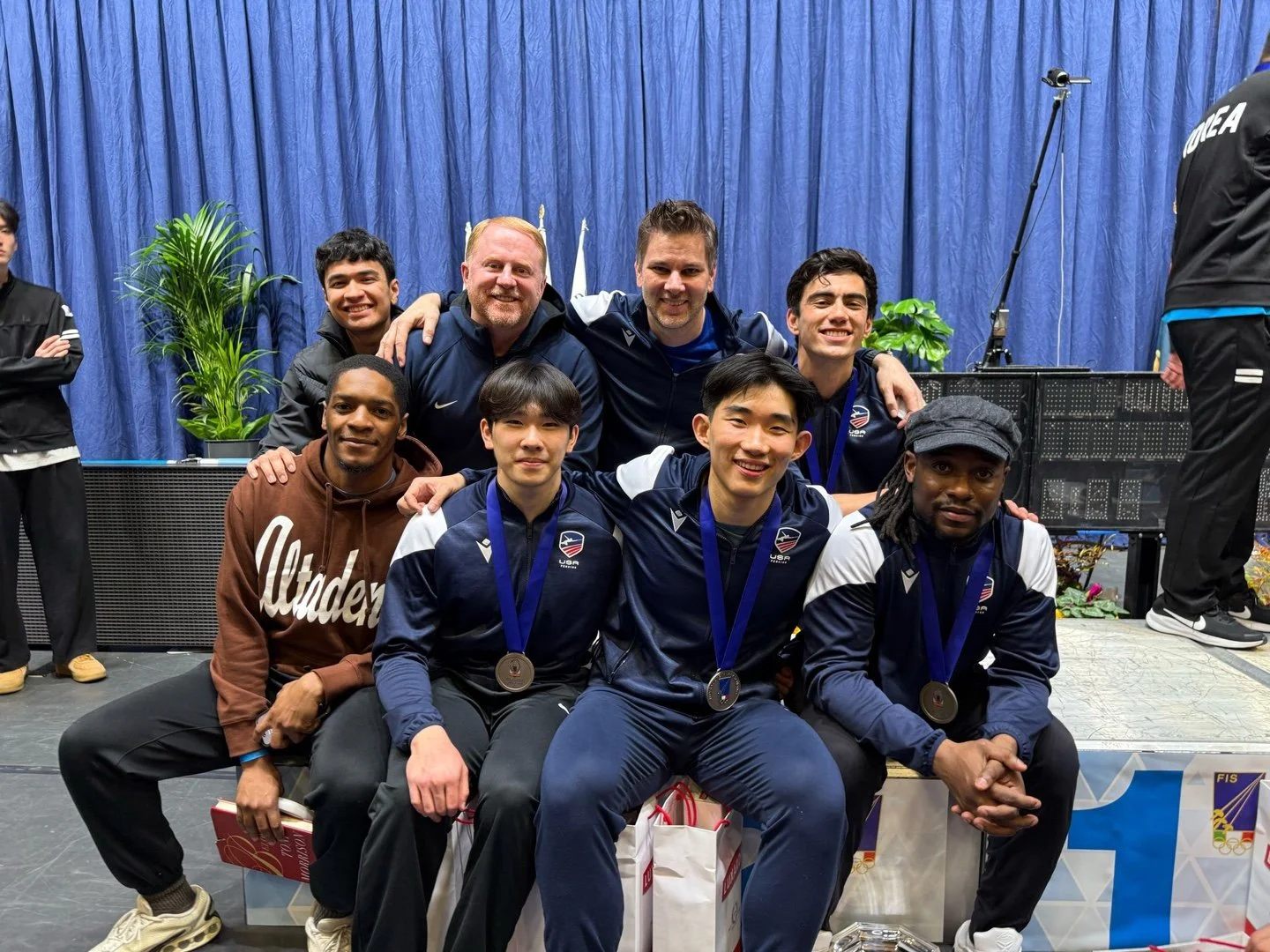 Group of diverse athletes and coaches on a podium with medals and a blue curtain background