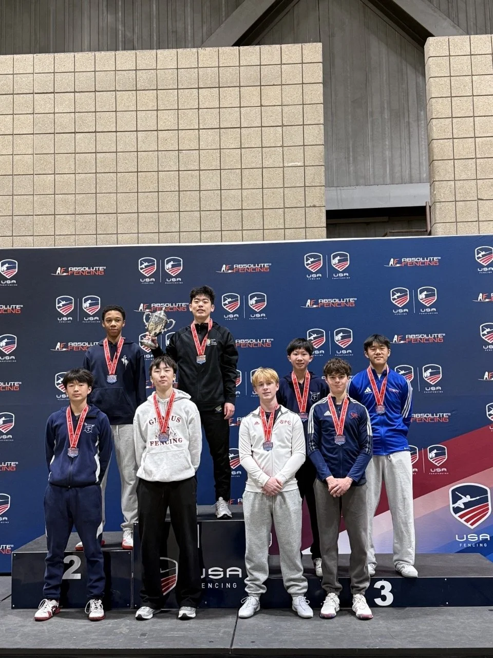 Group of male fencing athletes on the podium holding medals and certificates at the 2025 Summer Nationals in Milwaukee, Wisconsin.