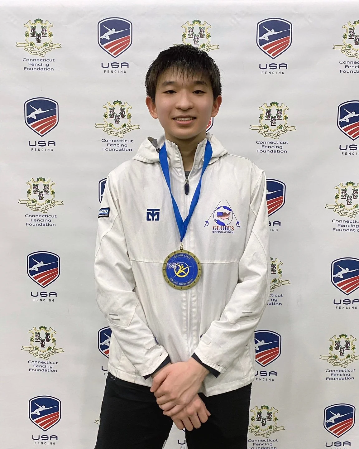 Young male fencer with medal stands near backdrop with USFA and Connecticut Fencing Foundation logos.