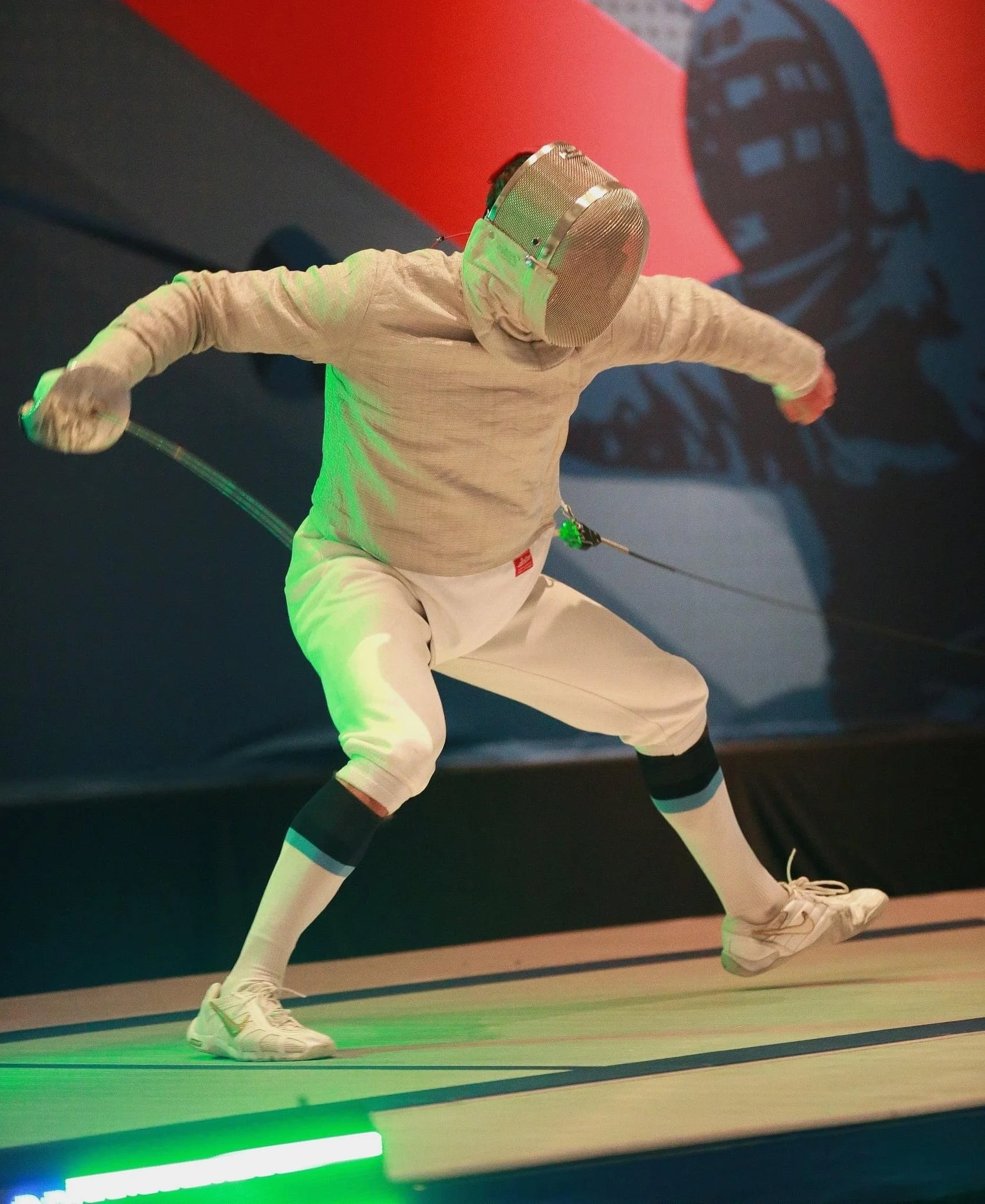 Fencing athlete in gear performing a lunge attack with foil saber in competition.