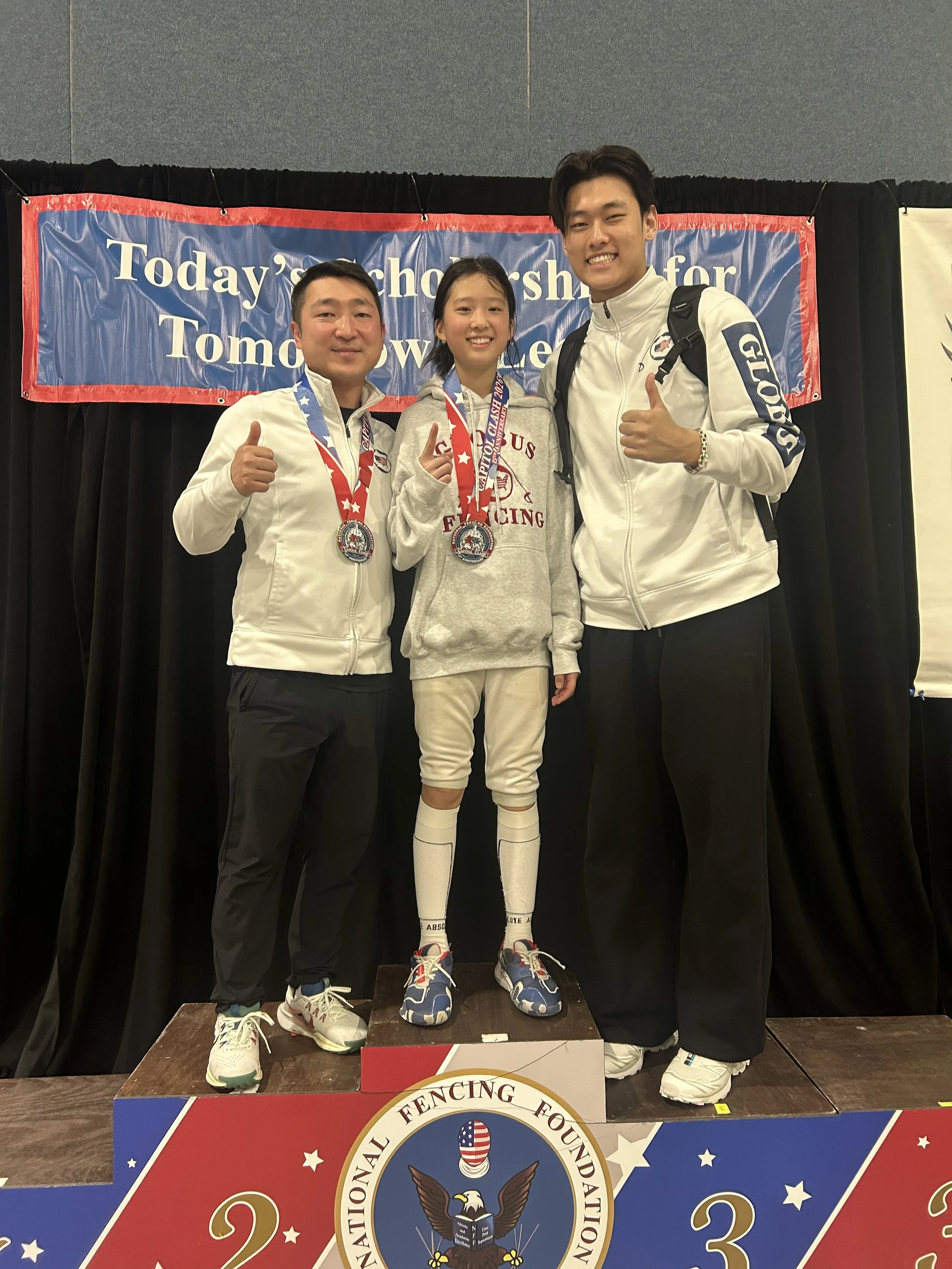 Three athletes standing on a winners' podium, wearing medals, with a banner in the background that says 'Today’s Scholarship for Tomorrow’s Leader.'
