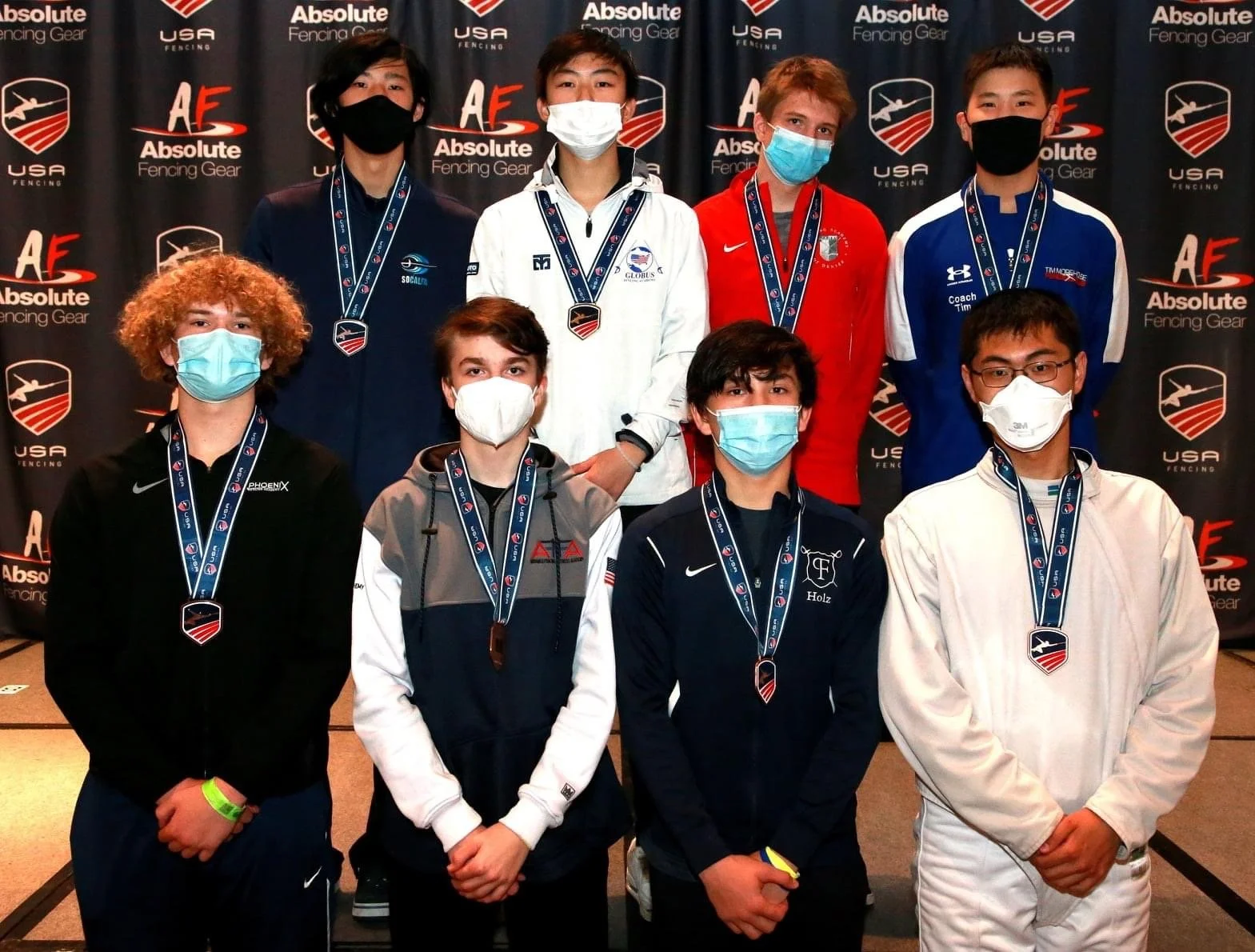 Group of nine young people wearing face masks and medals, posing for a photo at a fencing event. The backdrop features logos for USA Fencing Gear and Absolute Fencing Gear.