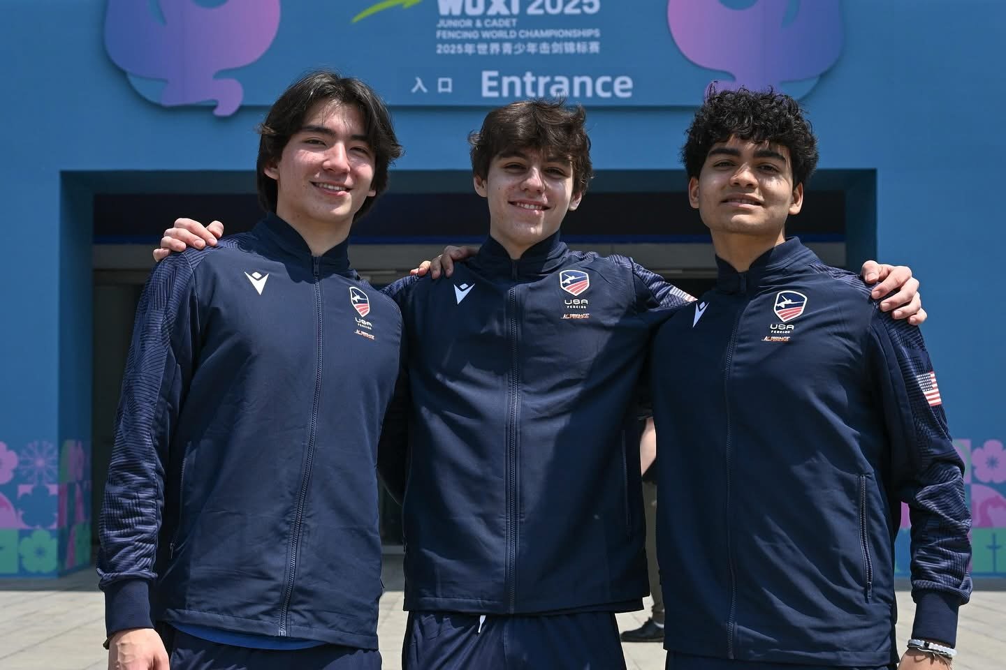 Three young men in matching USA Fencing team jackets standing together with arms around each other's shoulders, smiling at a fencing event entrance.