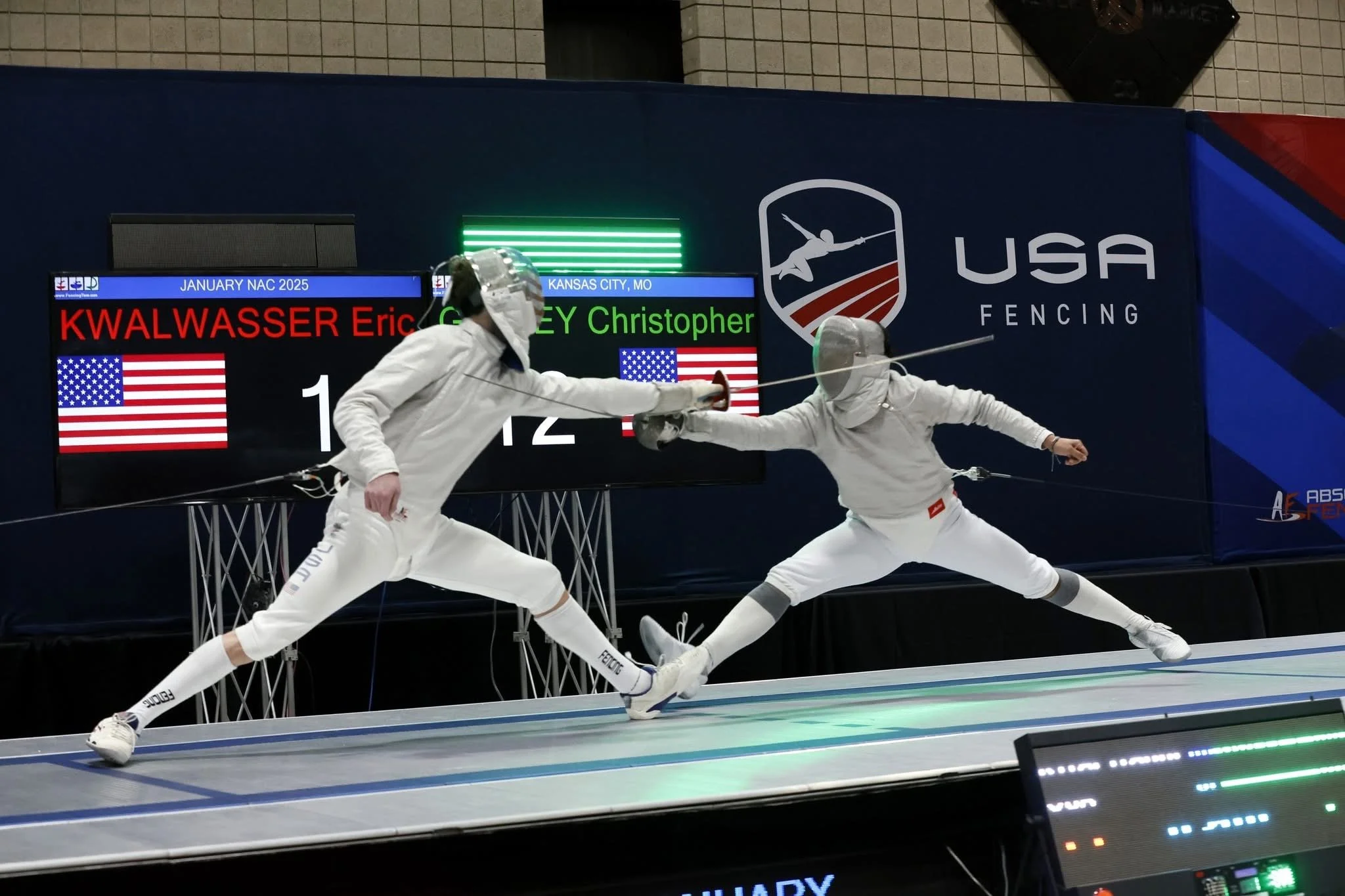 Two fencers in white protective gear fencing each other during a match at a USA fencing competition.
