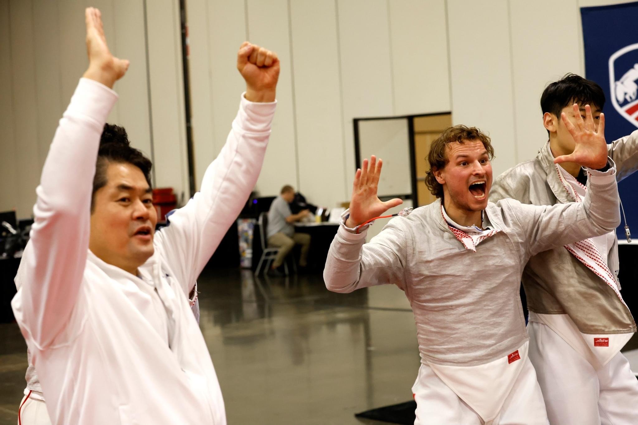 Three men celebrating with their arms raised, smiling and cheering, in an indoor setting.