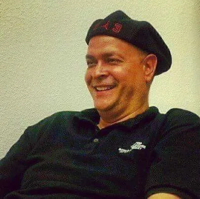 Man smiling, wearing a black beret with red embroidery and a black polo shirt.