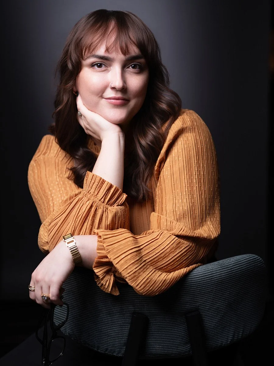 Kait seated in a rust-colored blouse against a dark studio background