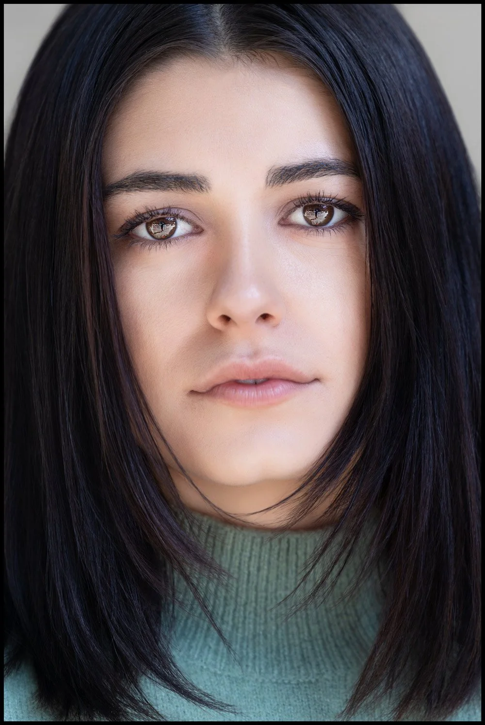 Close-up of a young woman with straight black hair and brown eyes, wearing a green top.
