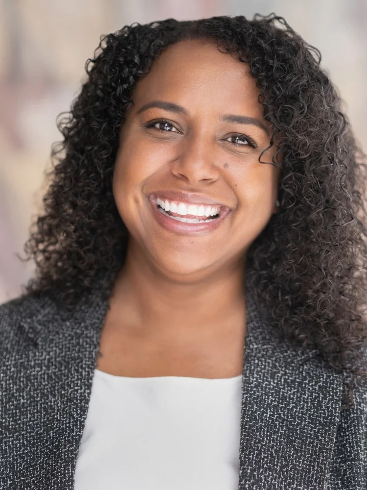 Smiling woman with curly hair in a gray blazer and white top