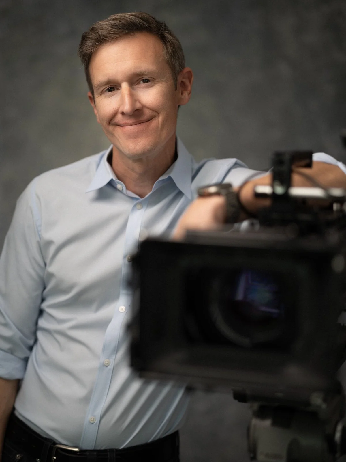 Man smiling at camera in a professional setting, with a camera in the foreground.