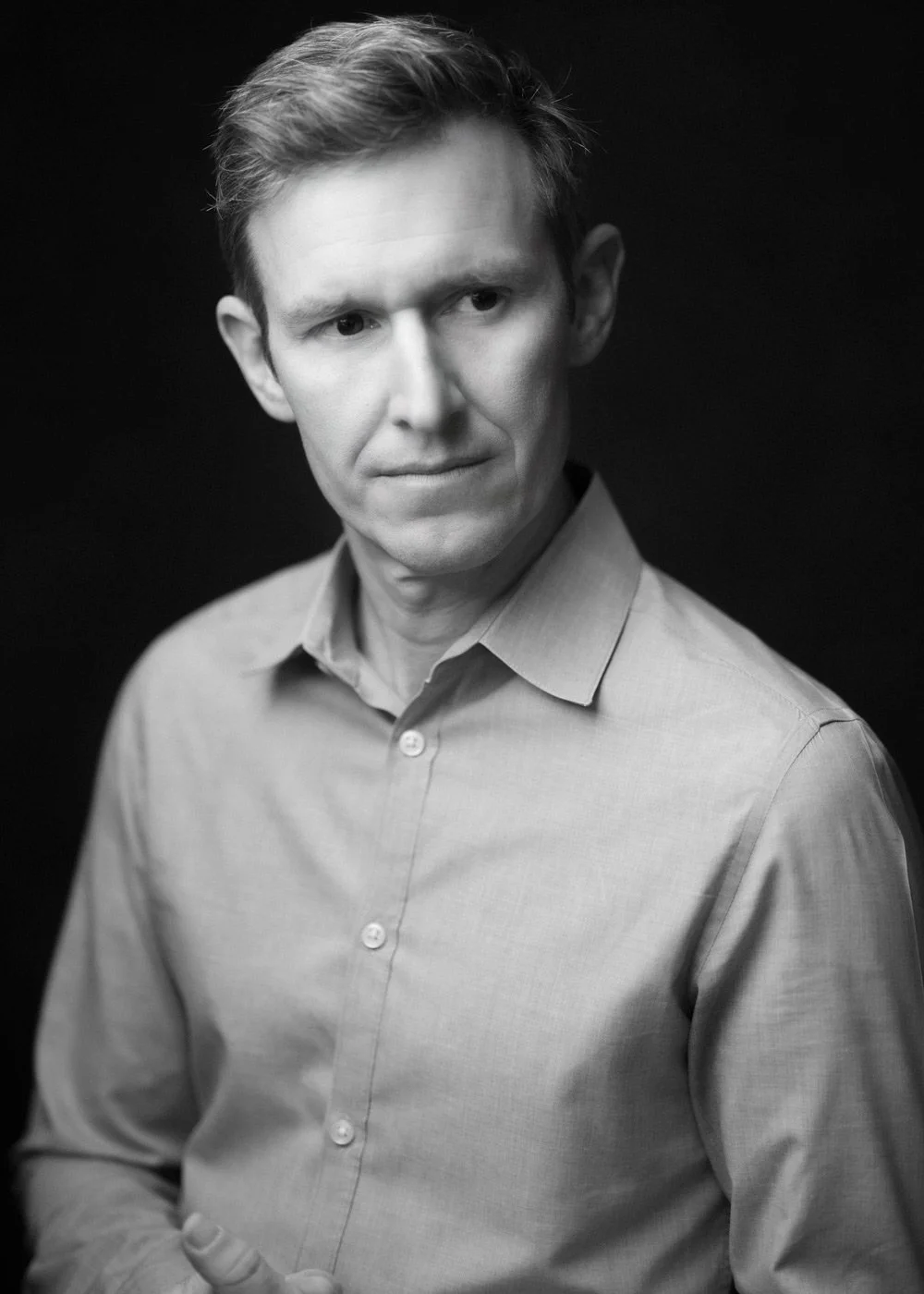 Black and white portrait of a man in a collared shirt, looking to the side against a dark background.
