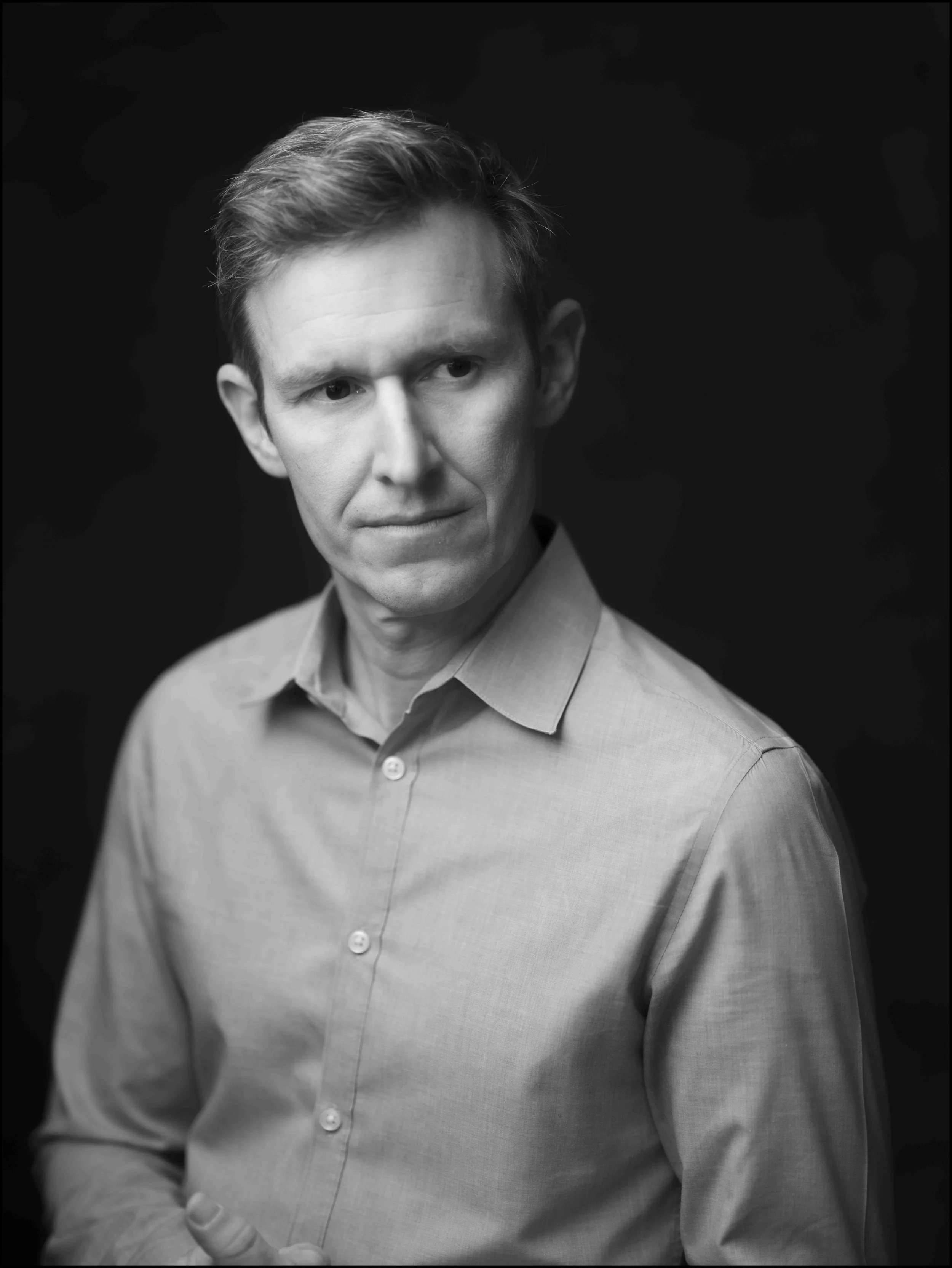 Black and white portrait of a man with light-colored hair, wearing a button-up shirt, looking to his left with a serious expression.