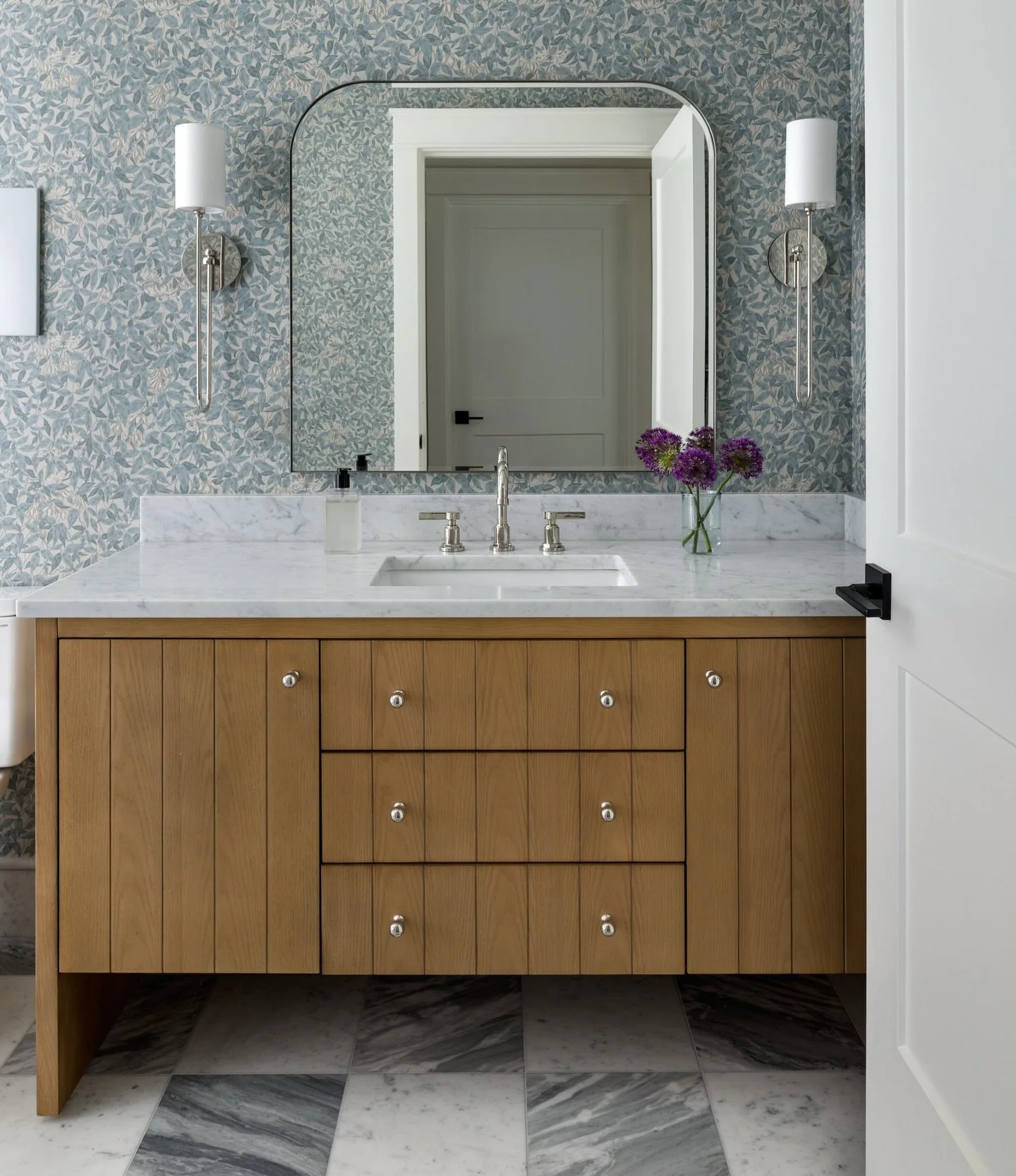 Some spaces come together quietly, and that&rsquo;s part of their strength. This bathroom is all about balance: a subtle wallpaper that softens the room, a tailored vanity that brings in warmth without demanding attention, and stone floors that add j