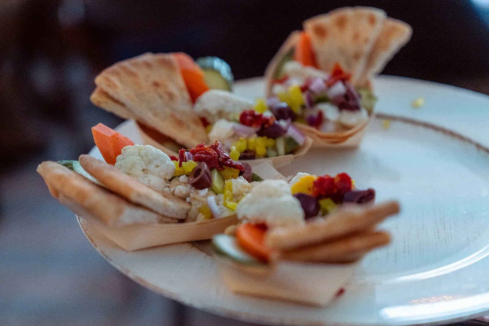 Three small serving boats with assorted vegetables and crackers on a white plate.