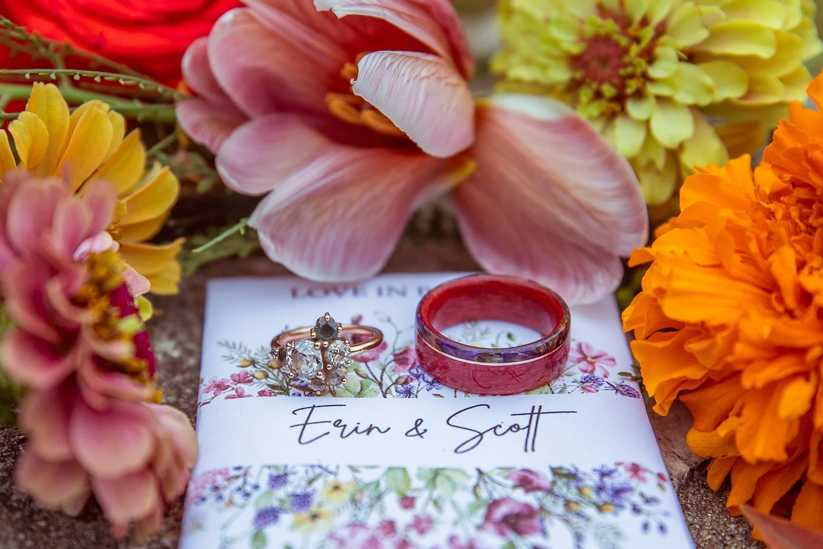 Wedding rings placed on a floral card with pink and orange flowers surrounding them.