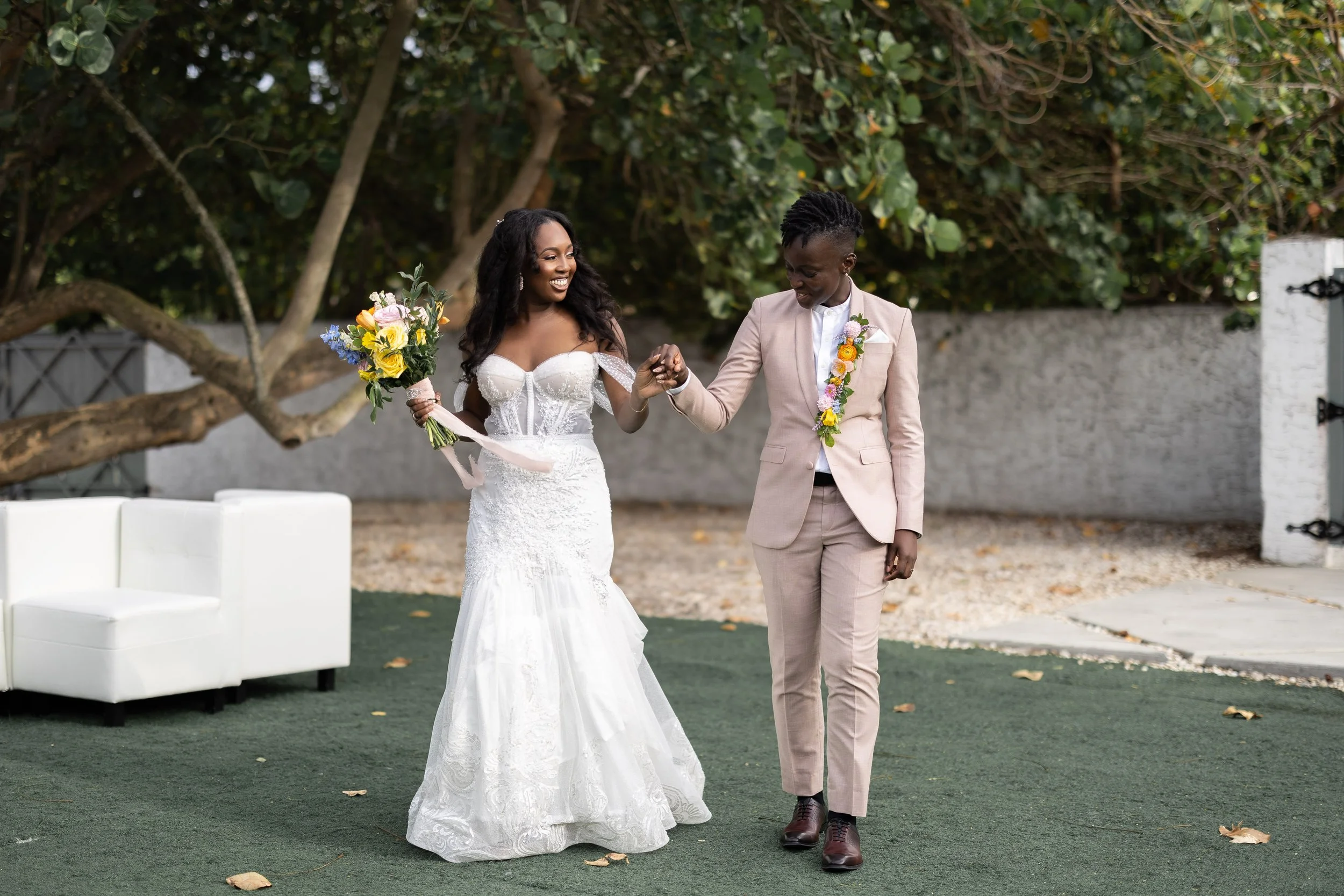 Joyful newlyweds walk hand in hand beneath lush tropical trees after their intimate garden wedding at The Rich Hippies House in South Florida, photographed by Alekandra London of Nine One Four & Co.