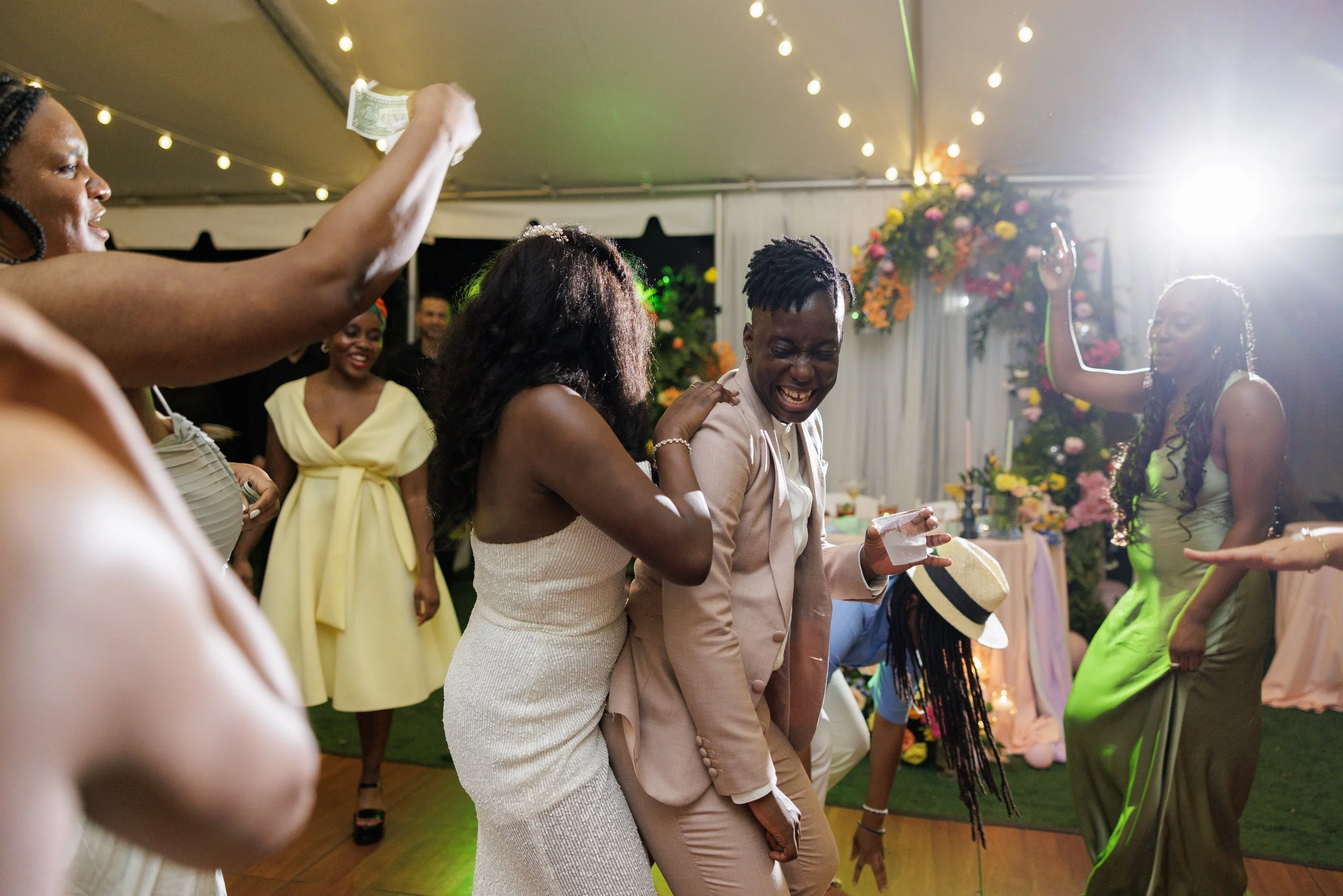 People dancing and celebrating at a party with colorful decorations and floral arrangements.