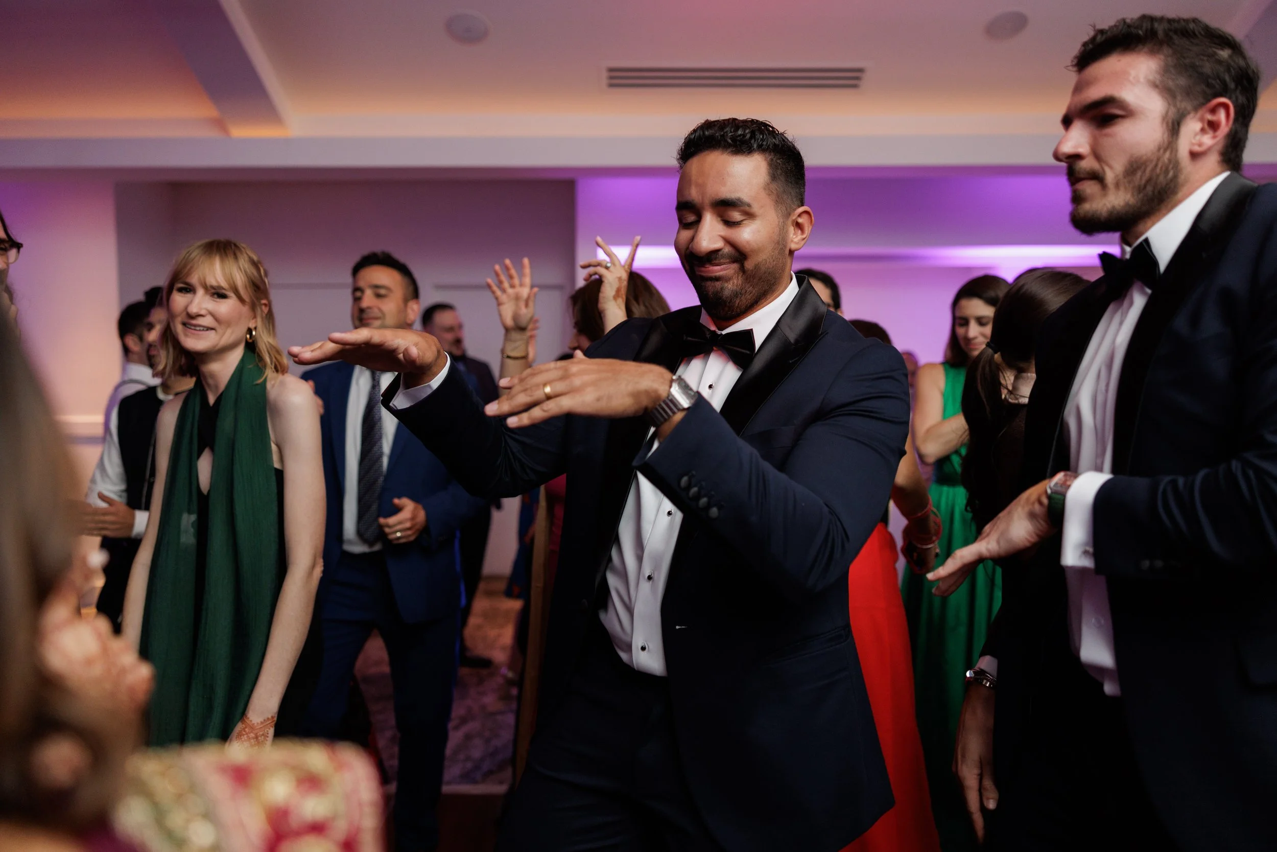 People dancing and enjoying at a formal party or event, with colorful lighting and elegant attire.