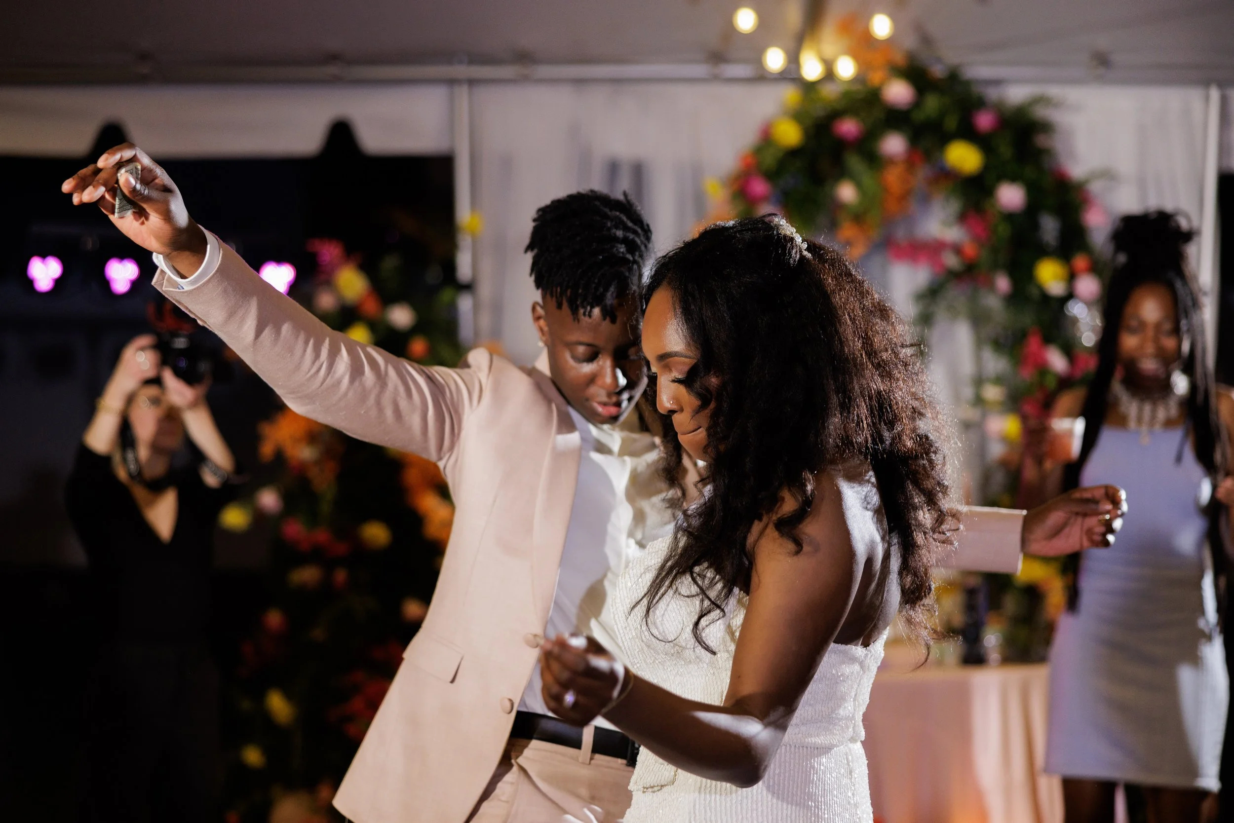 Two women dancing at a celebration with a floral backdrop
