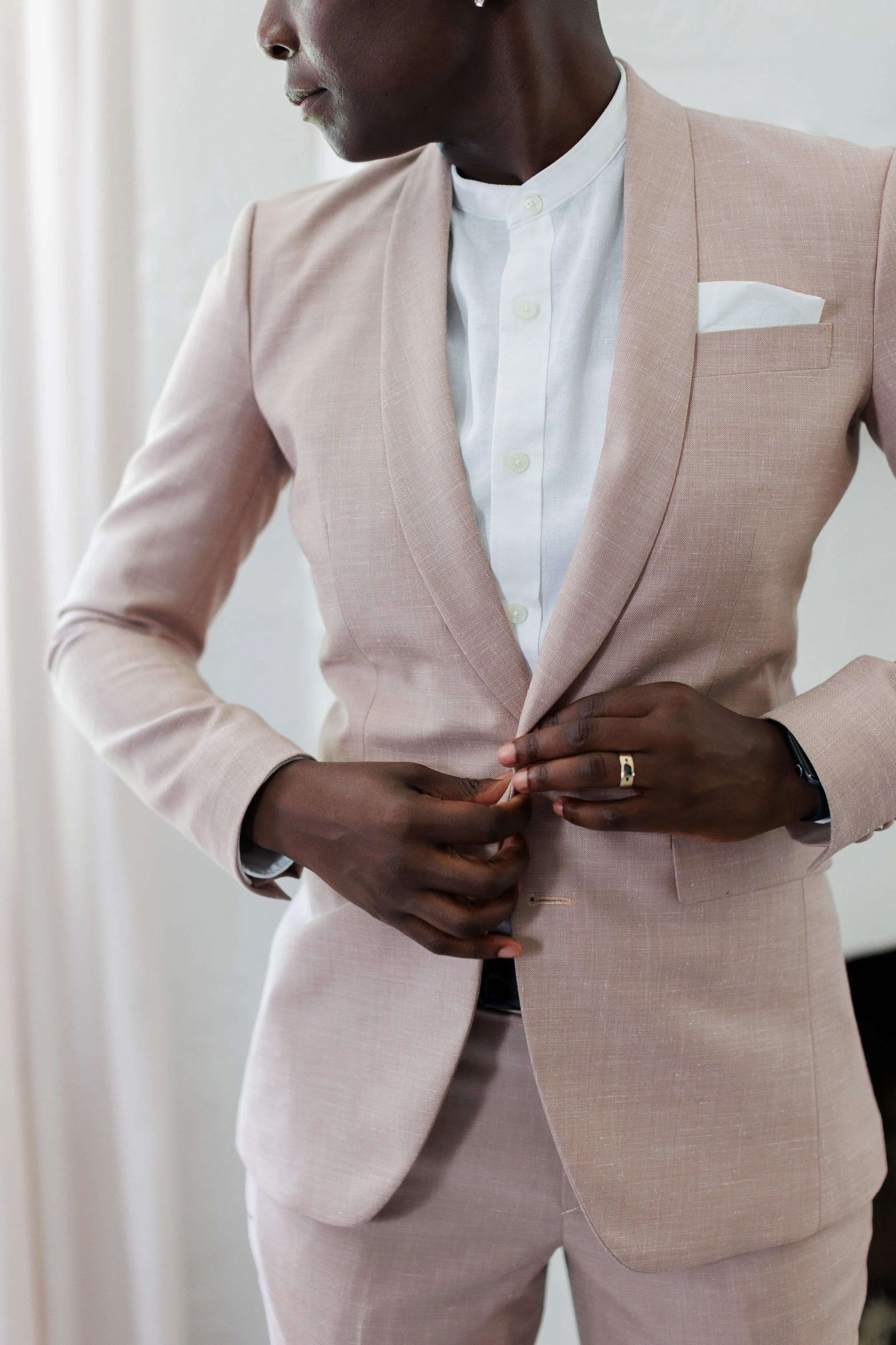 Person adjusting a light pink suit jacket over a white shirt, with a pocket square visible.
