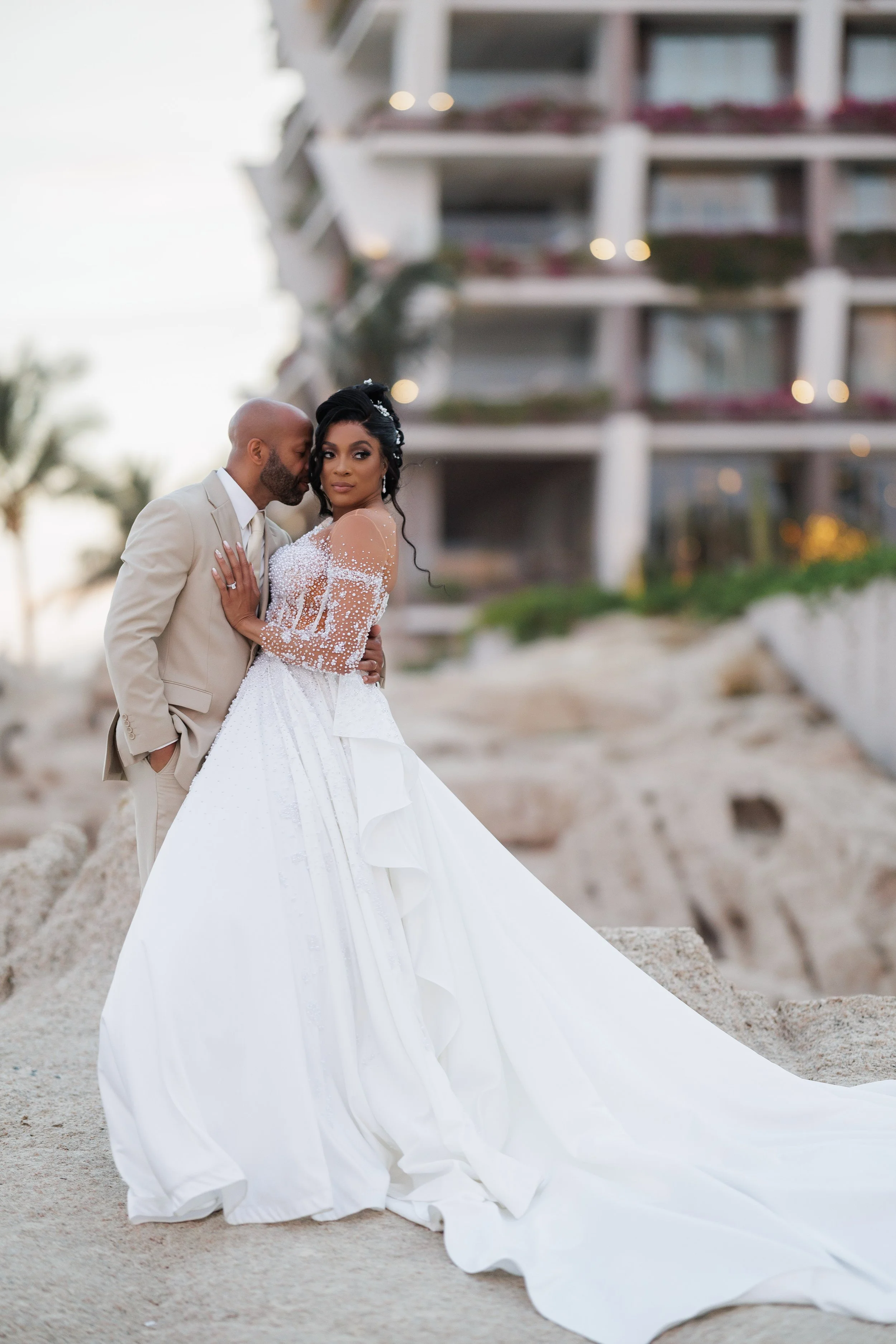 Couple embraces on the coastal rocks at Grand Velas Los Cabos during their destination wedding, captured with a fine-art editorial approach by Nine One Four & Co.