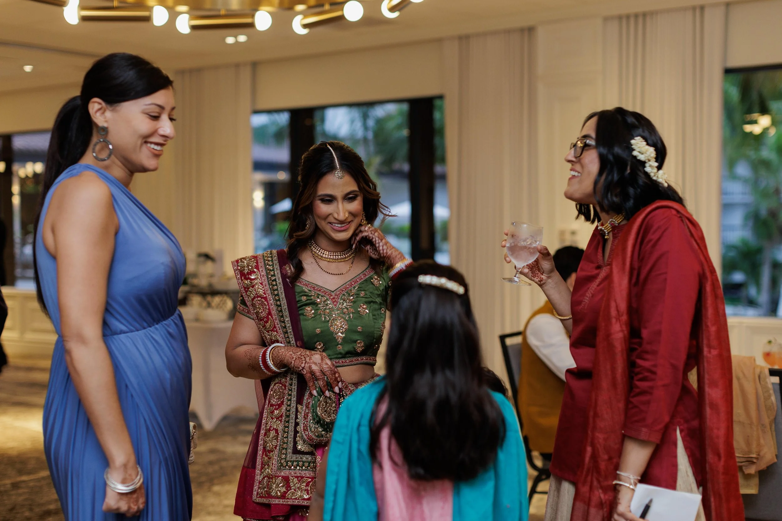Group of women in traditional Indian attire smiling and chatting at an indoor event.