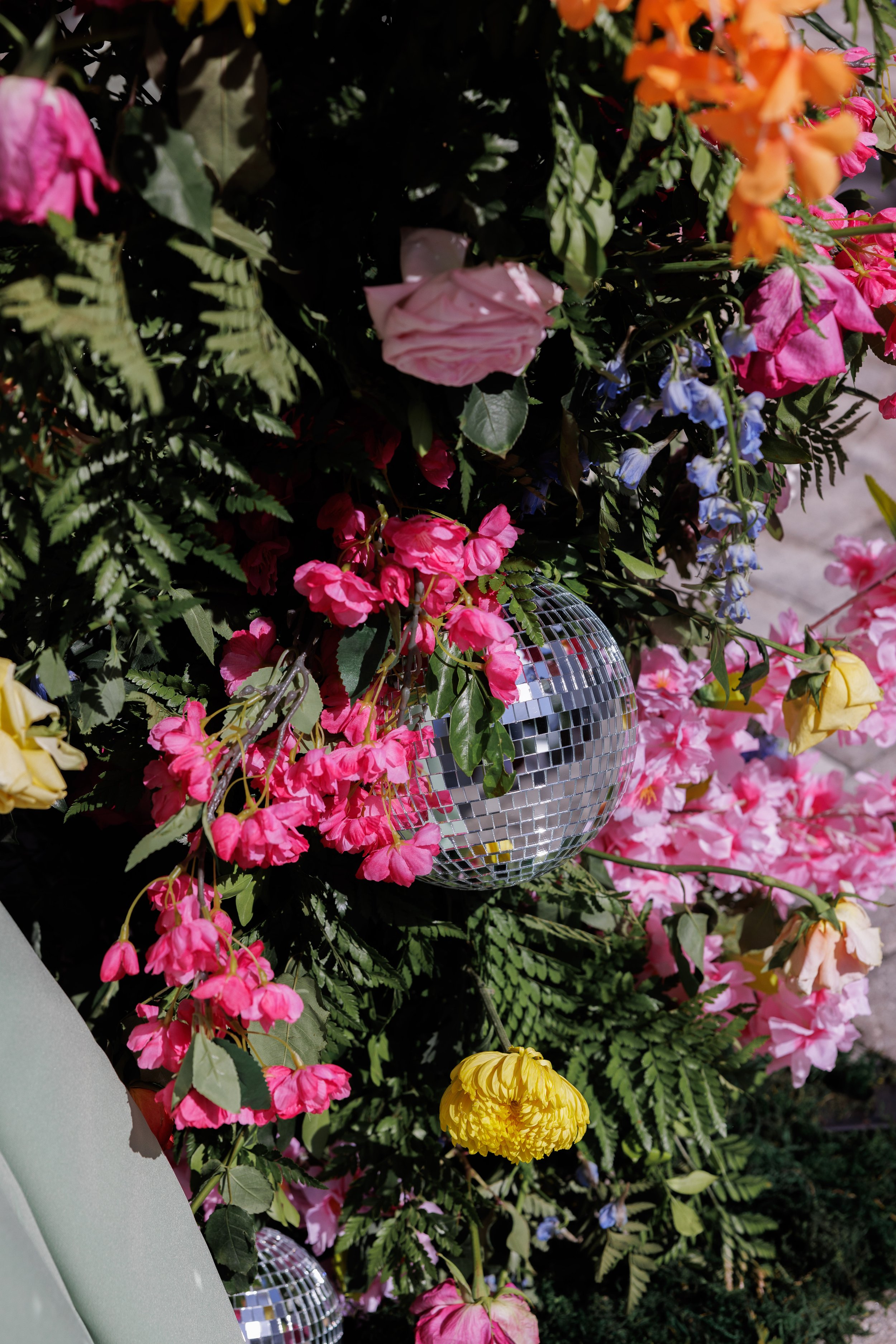Arrangement of colorful flowers, including pink, yellow, and purple blossoms, with a small disco ball among the flowers.