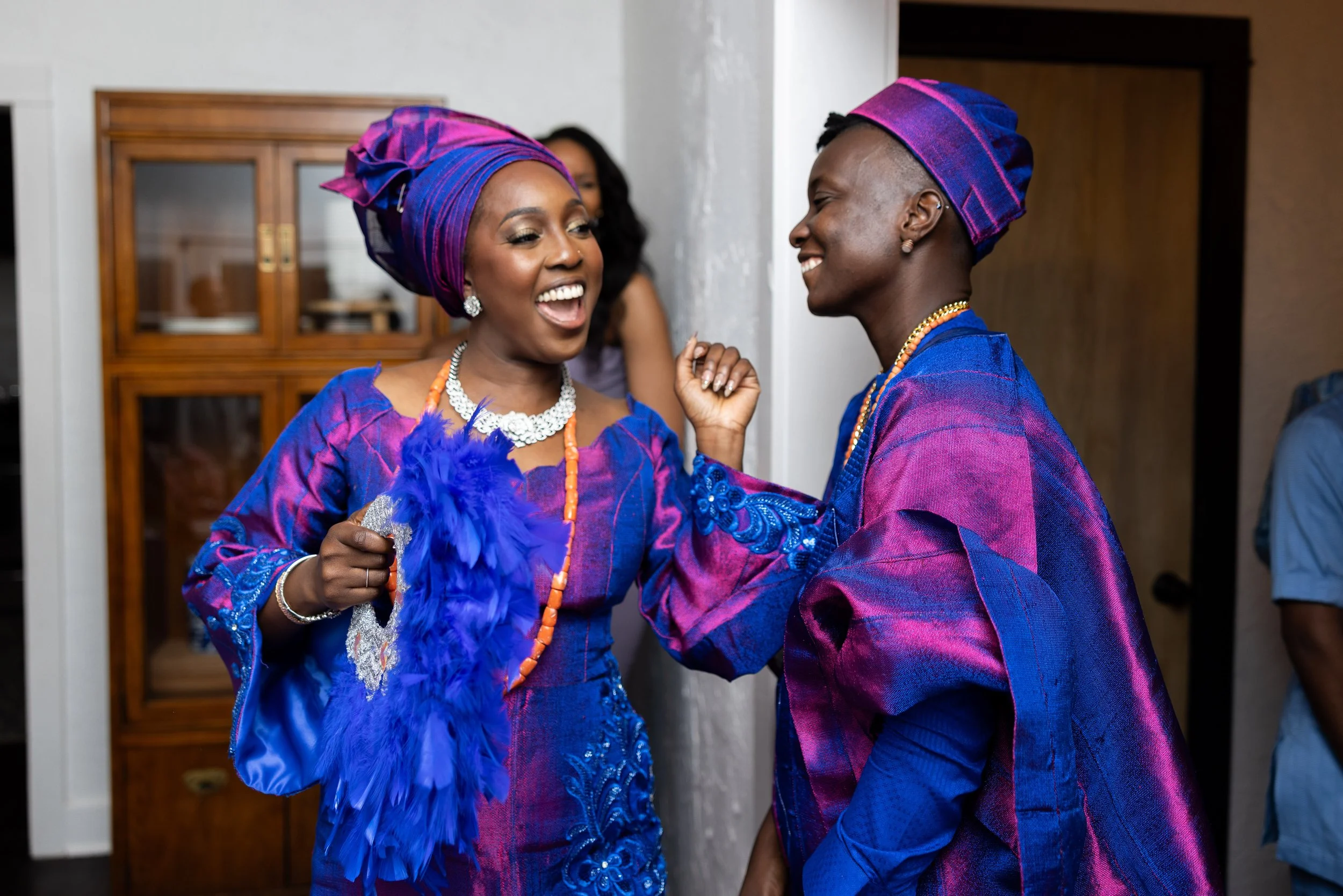 Two women dressed in vibrant traditional African attire, smiling and engaging in a joyful moment.