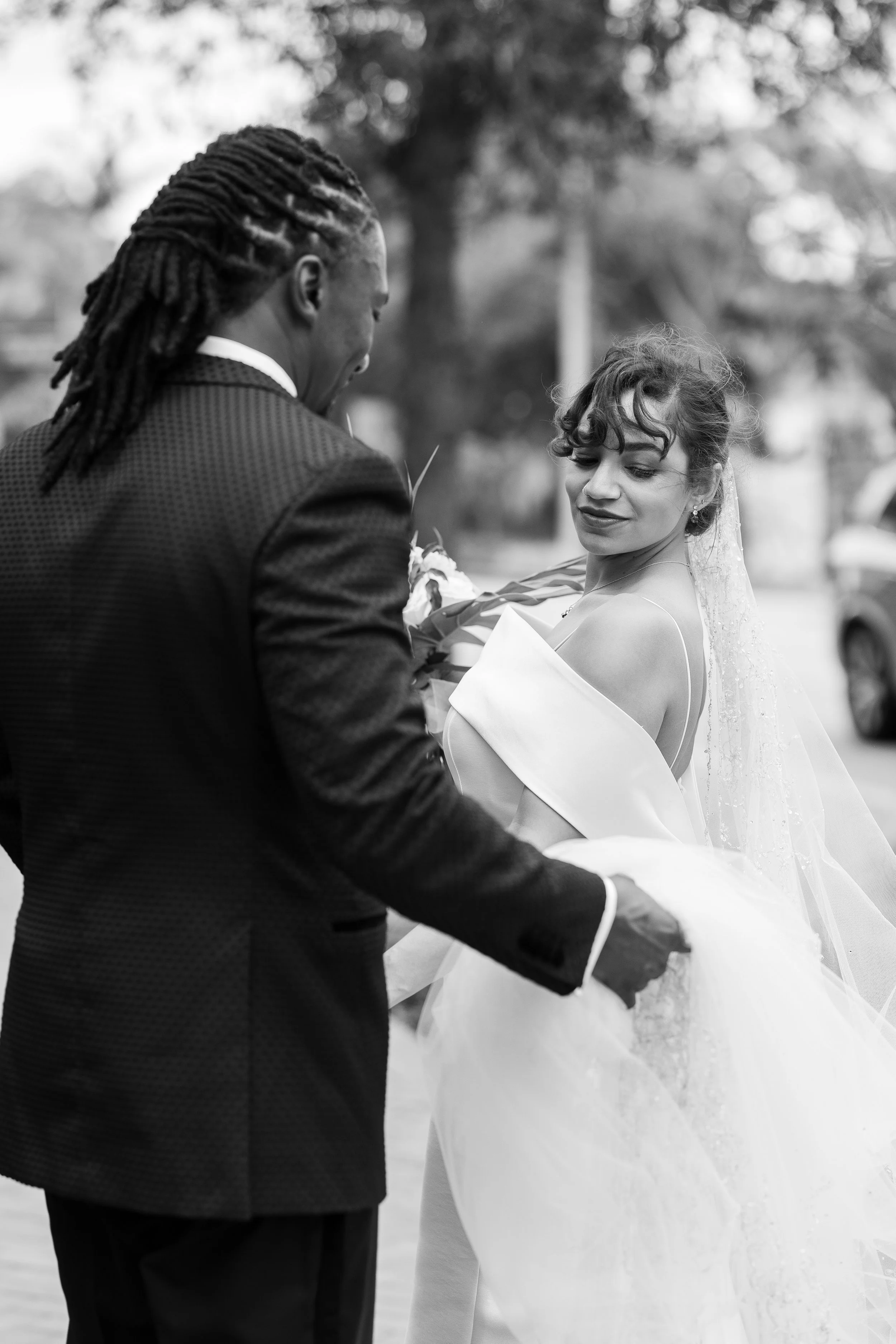 A man in a suit presents flowers to a woman in a wedding dress, outdoors, in black and white.