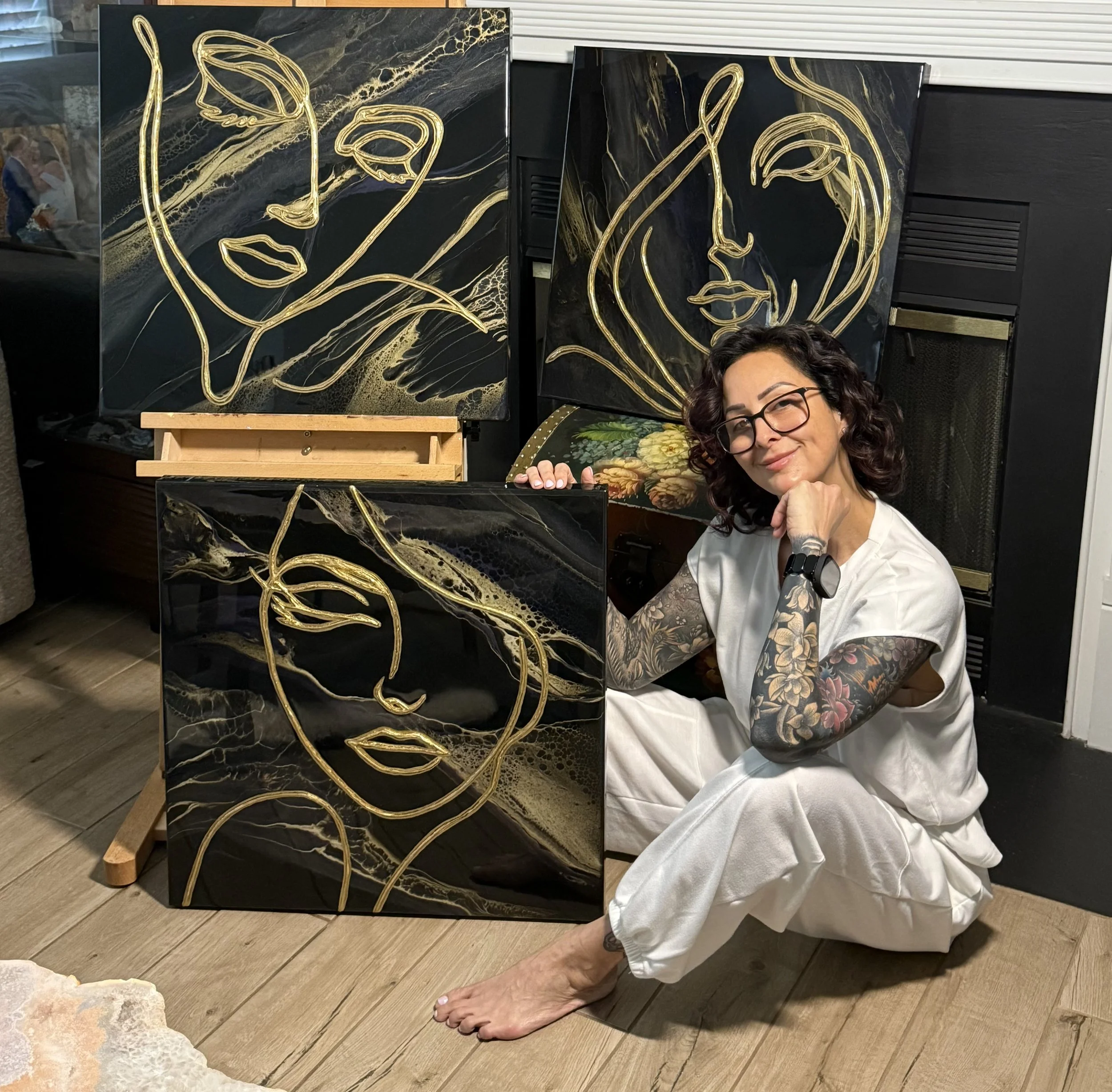 Tina Hursh-Emond with her Sacred Lines collection—minimalist gold line art of feminine faces layered over black and gold fluid art backgrounds, capturing healing, elegance, and emotional depth