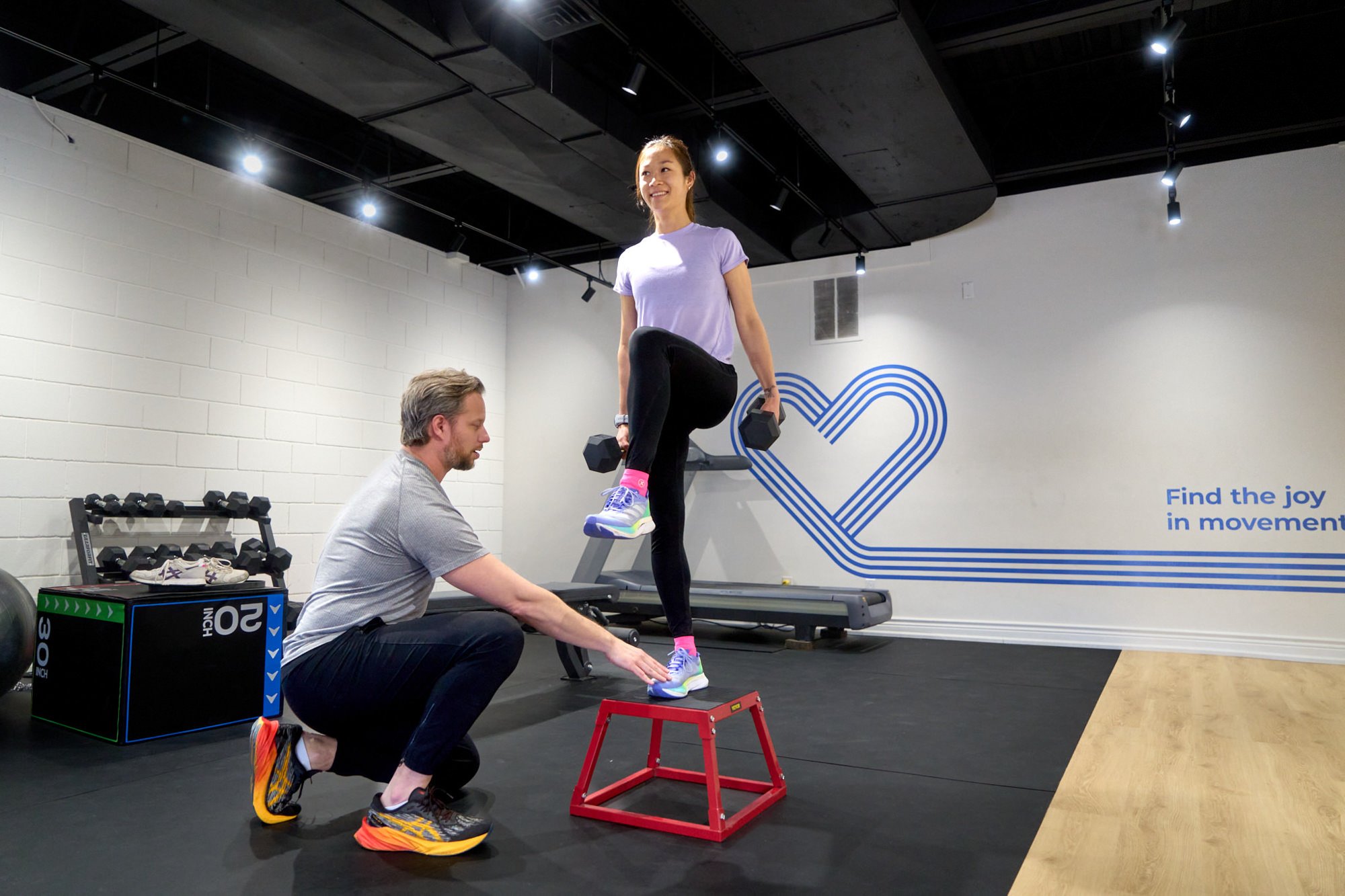 A physiotherapist working with a runner who is doing single-leg step-ups holding dumbbells