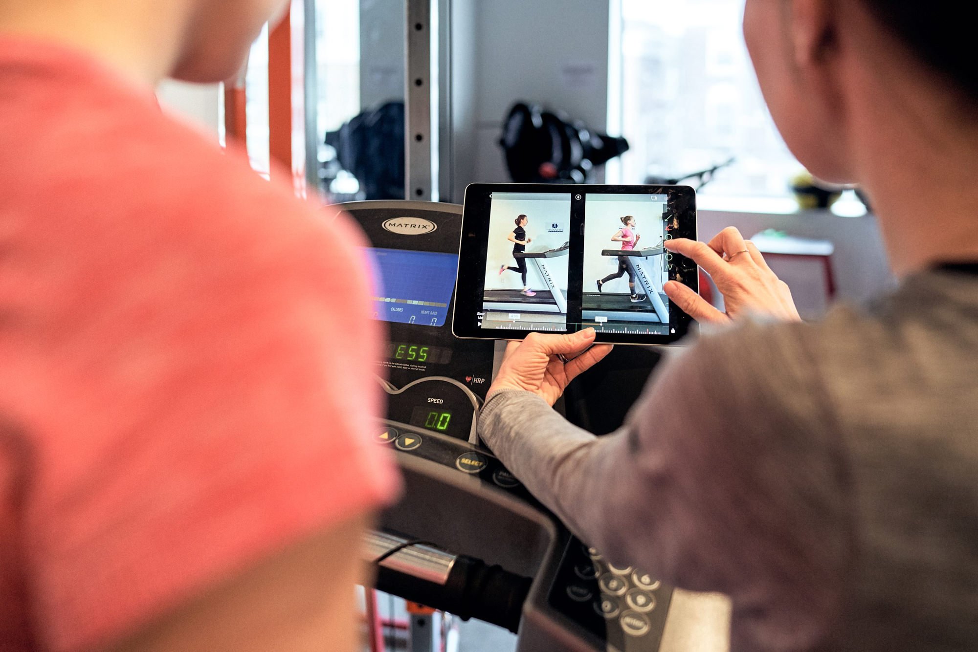 A physiotherapist conducting a gait analysis session using an iPad to discuss form with the patient