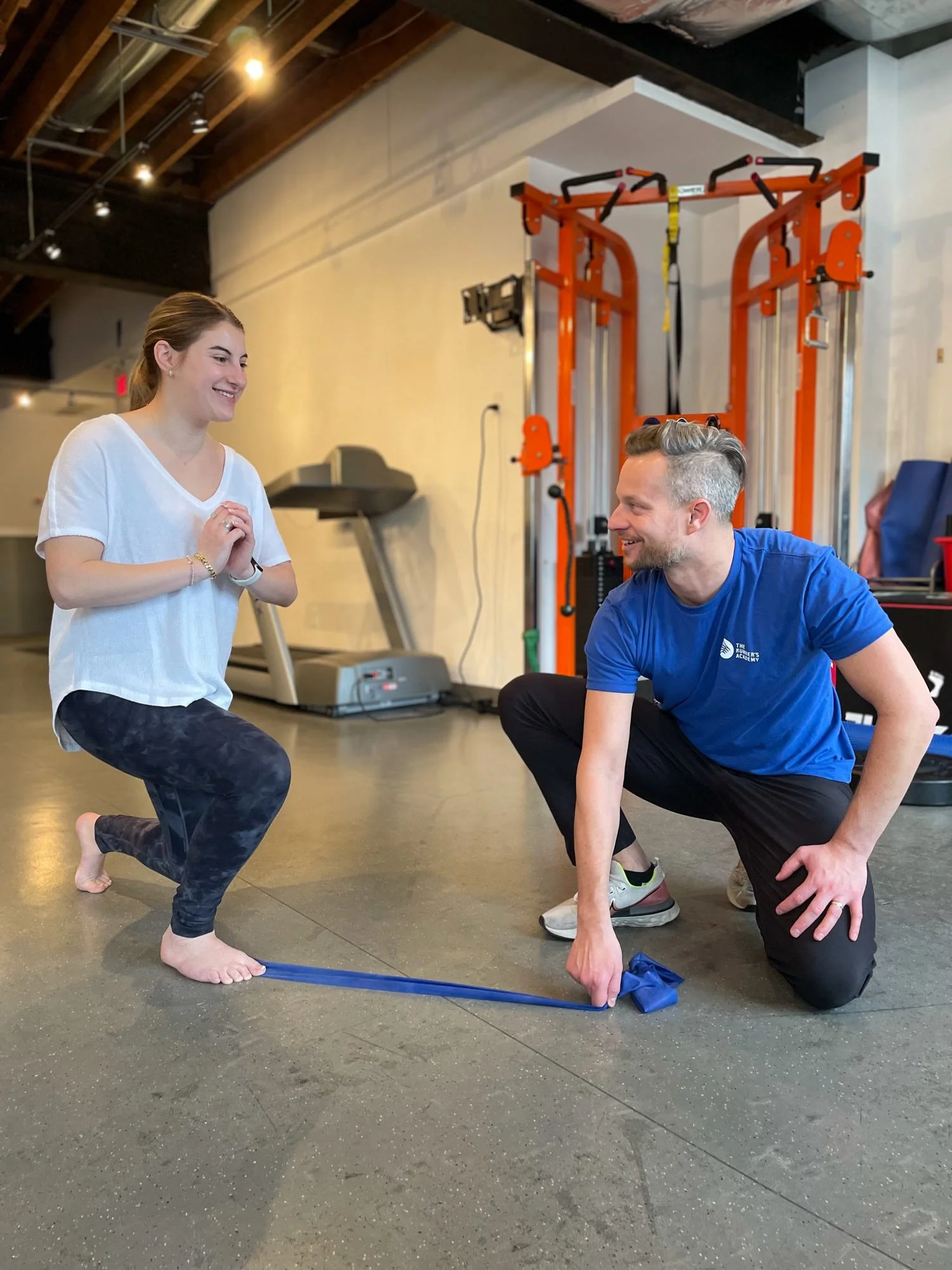 A physiotherapist using a TheraBand underneath the patient's foot to assist with proper alignment during lunges