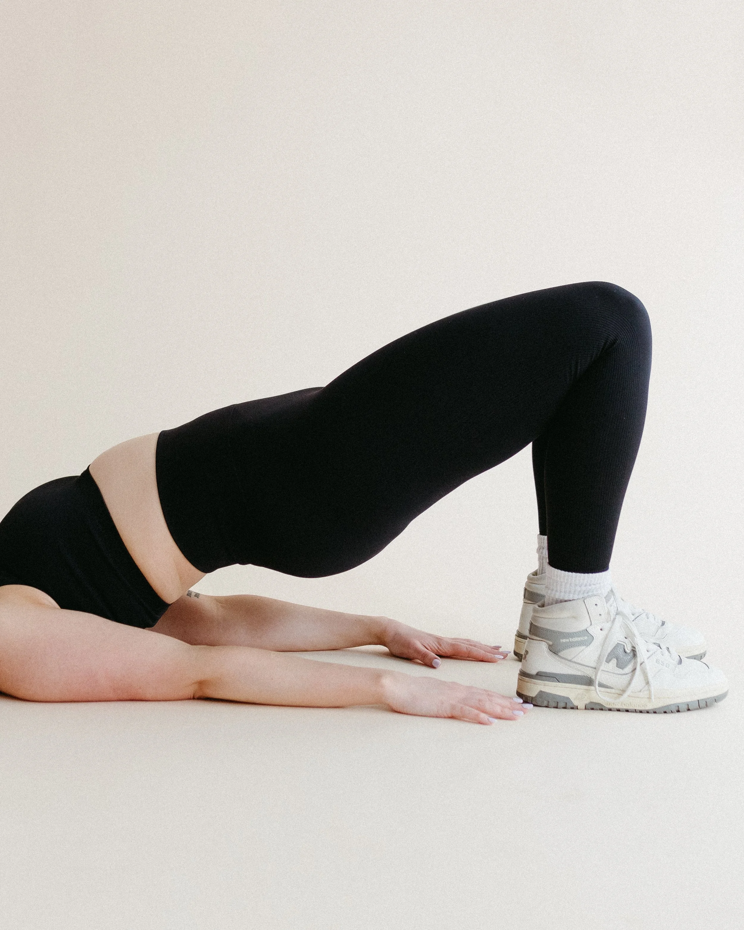 Two women in black athletic wear performing yoga or stretching exercises on a wooden floor.