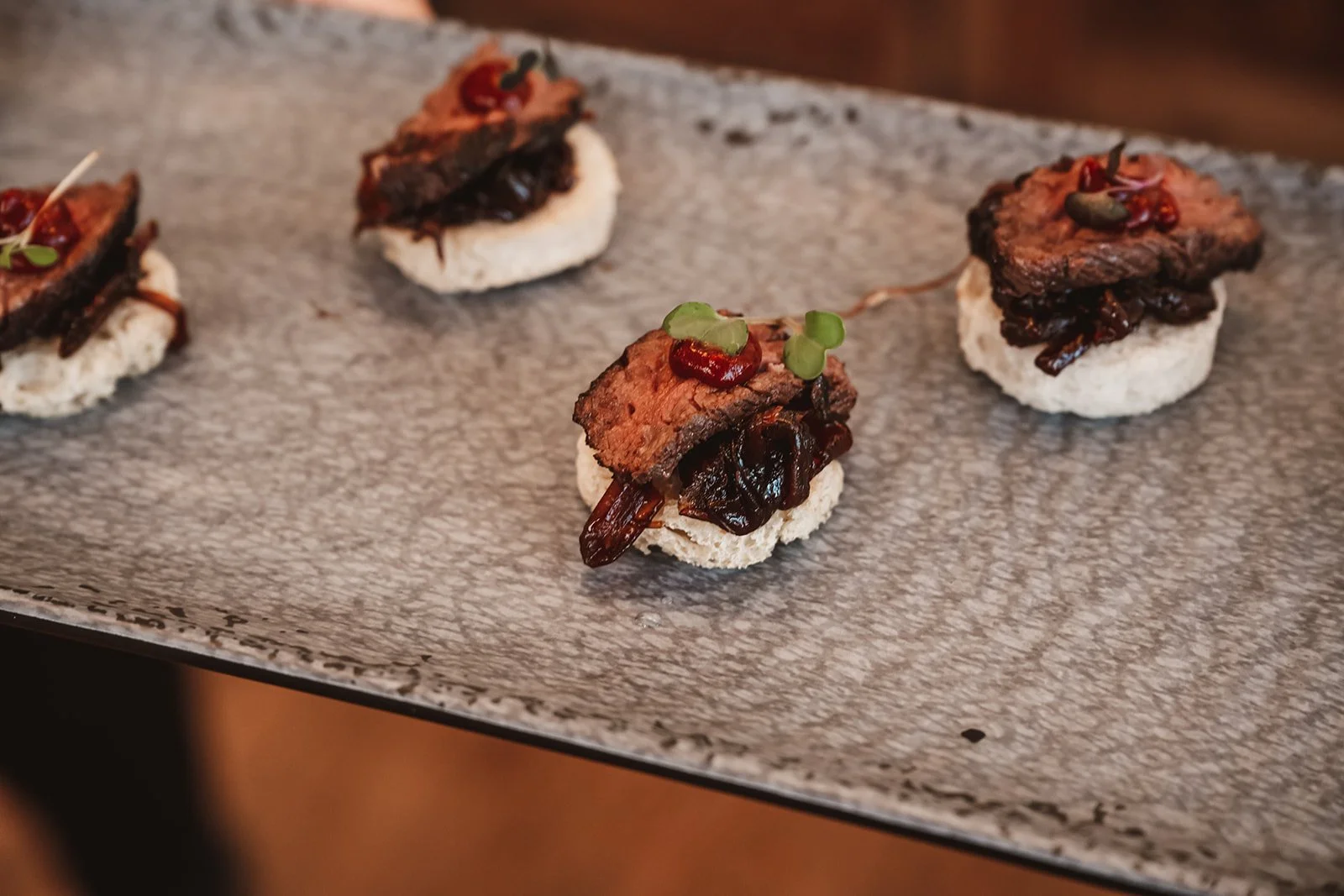 Short rib bites on ricer crackers with spicy red sauce on a marble platter.