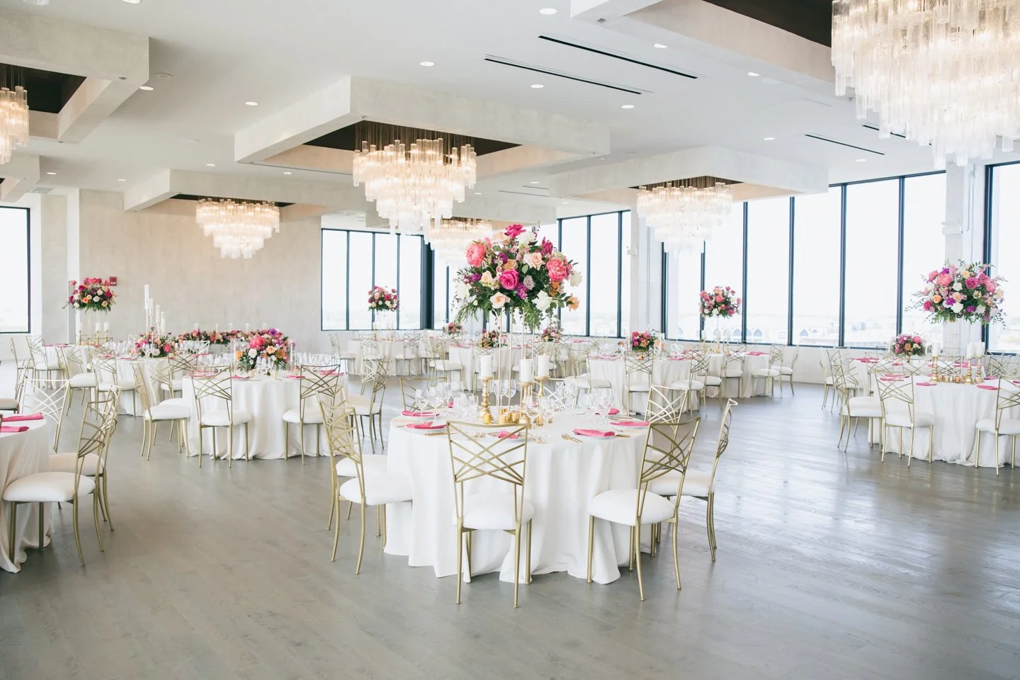 Event venue with round dinner tables and pink flowers and chandeliers.