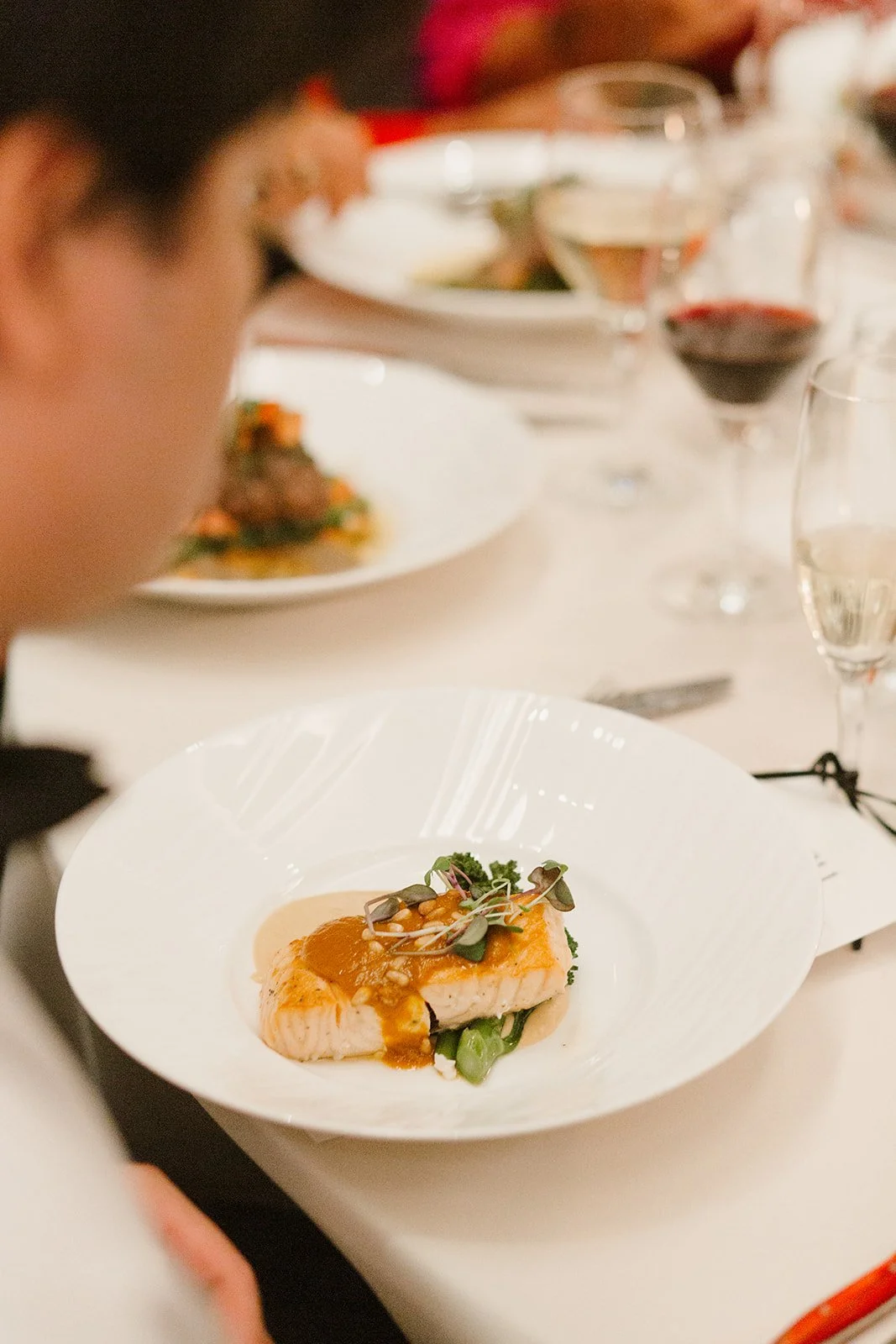Seared salmon on a round white plate with herbs and brown savory sauce.