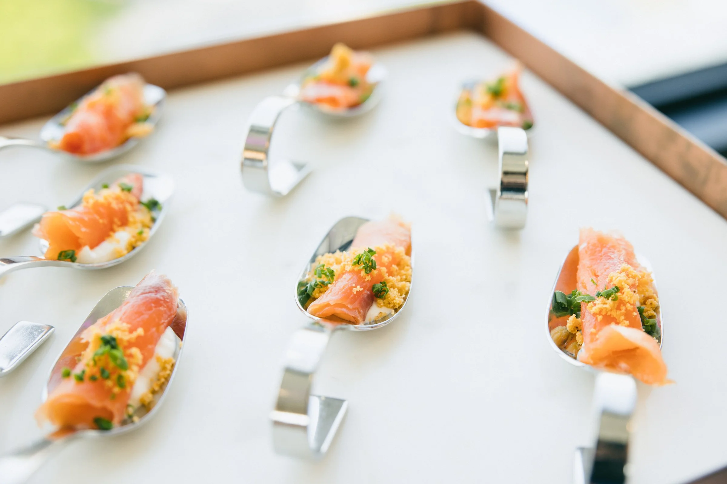 Smoked salmon bites served on individual serving spoons and white tray.