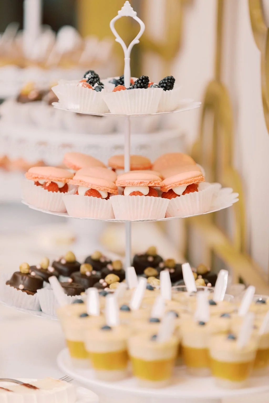 Desserts on a tiered serving platter with chocolates, pink macarons, berry tarts, and other sweets.