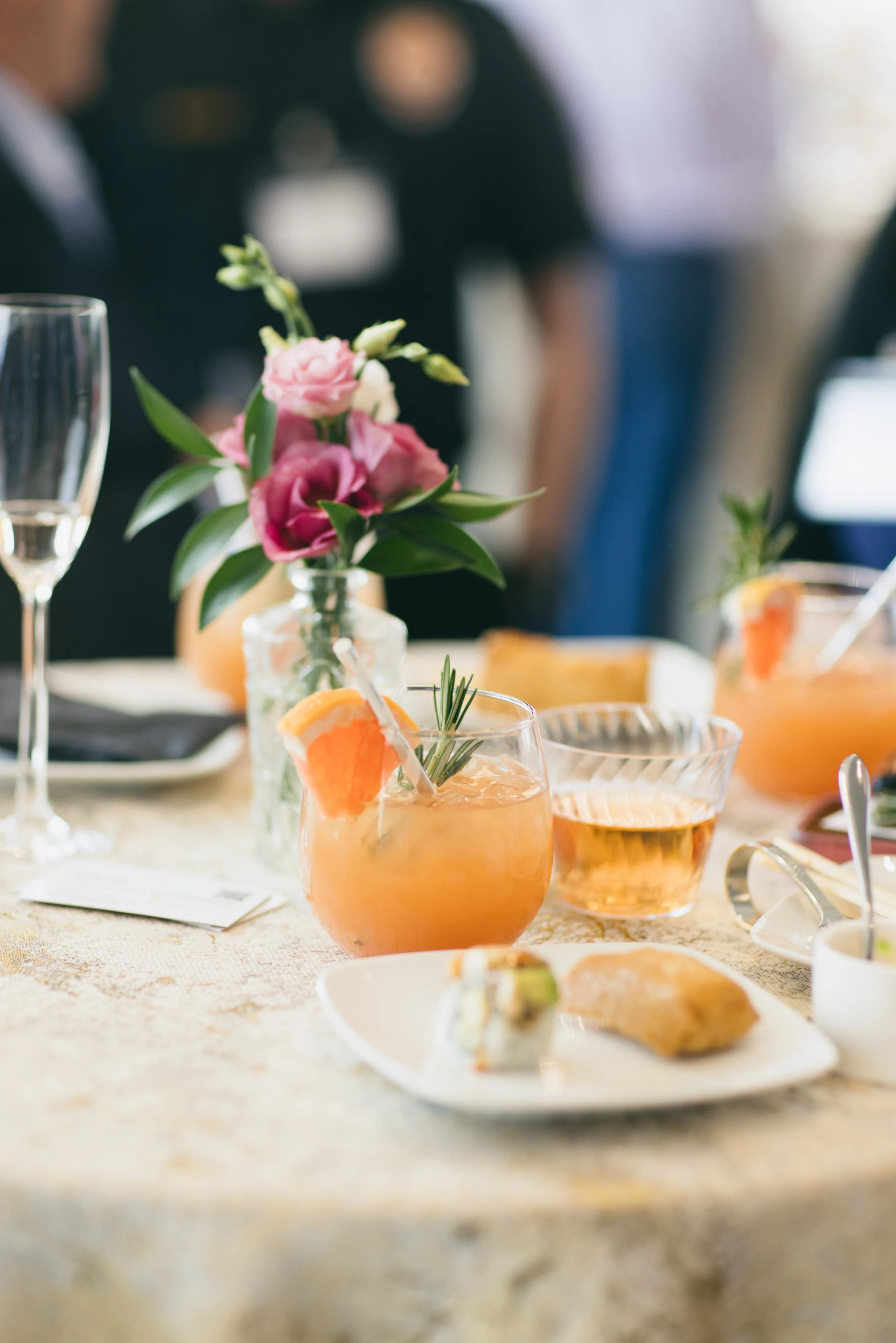 Paloma cocktail on a table with bites of food and flowers on the tables.