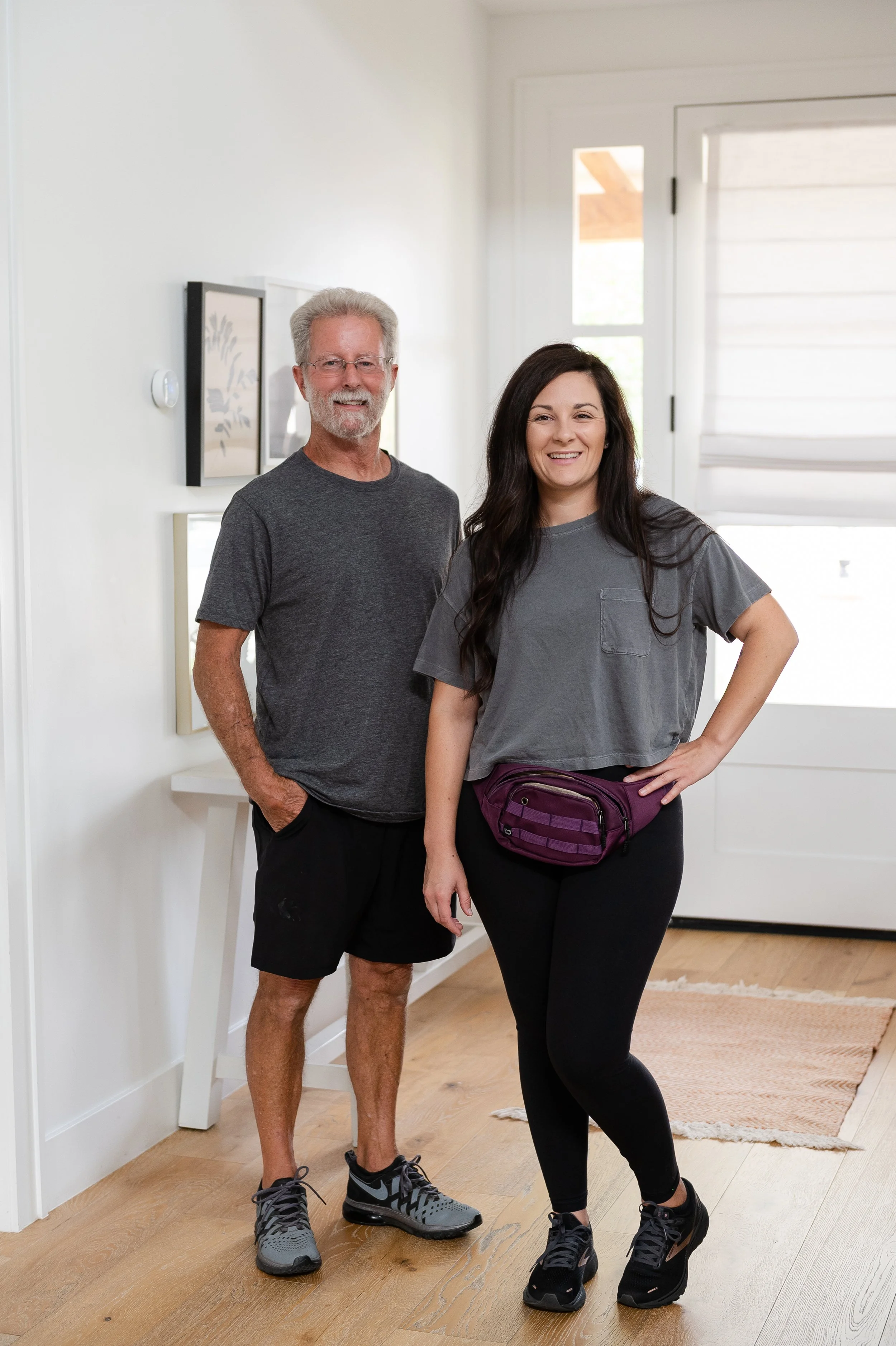 Older man and young woman stand inside a bright, modern home, smiling at the camera.
