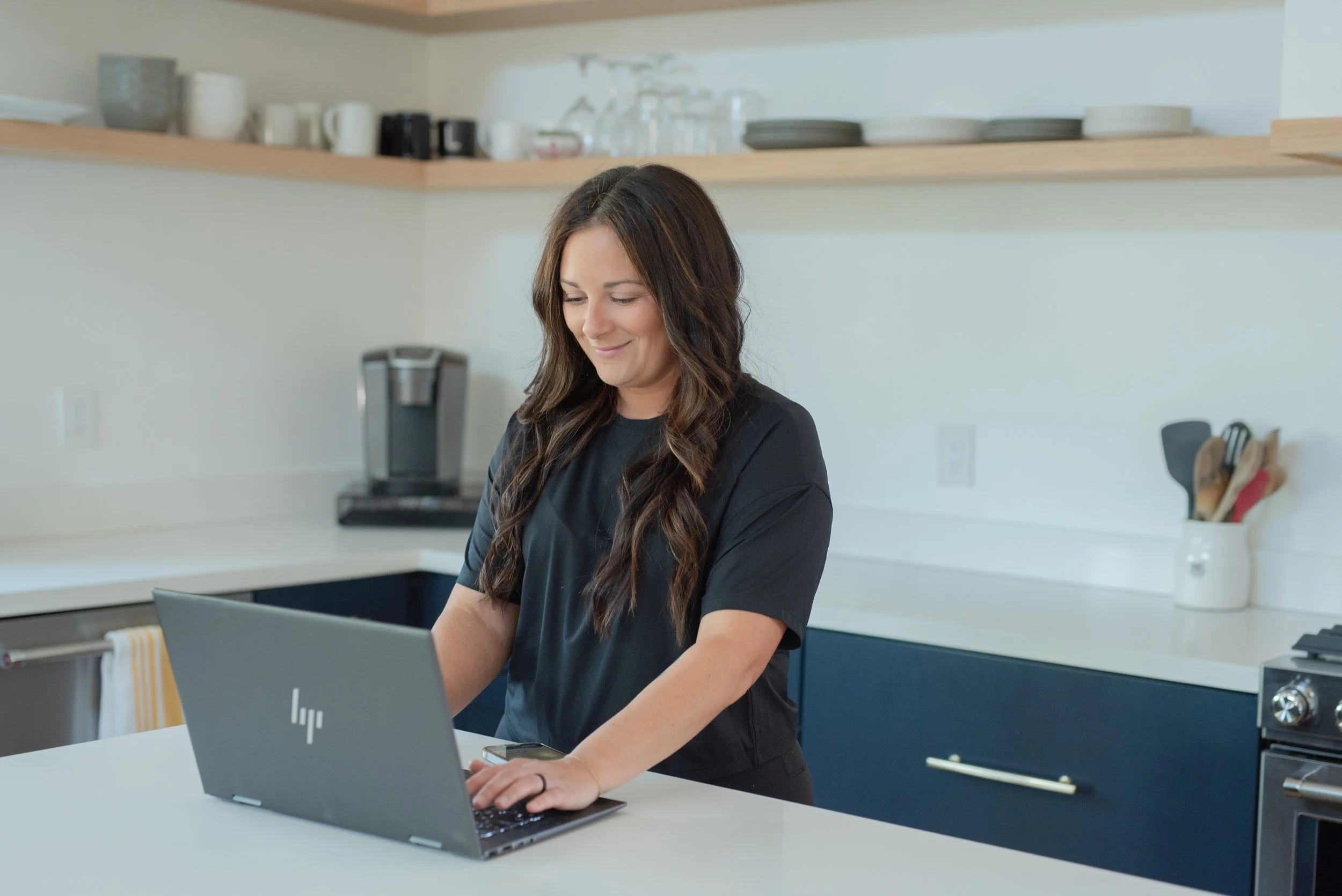Woman in black shirt using a laptop in a modern kitchen.
