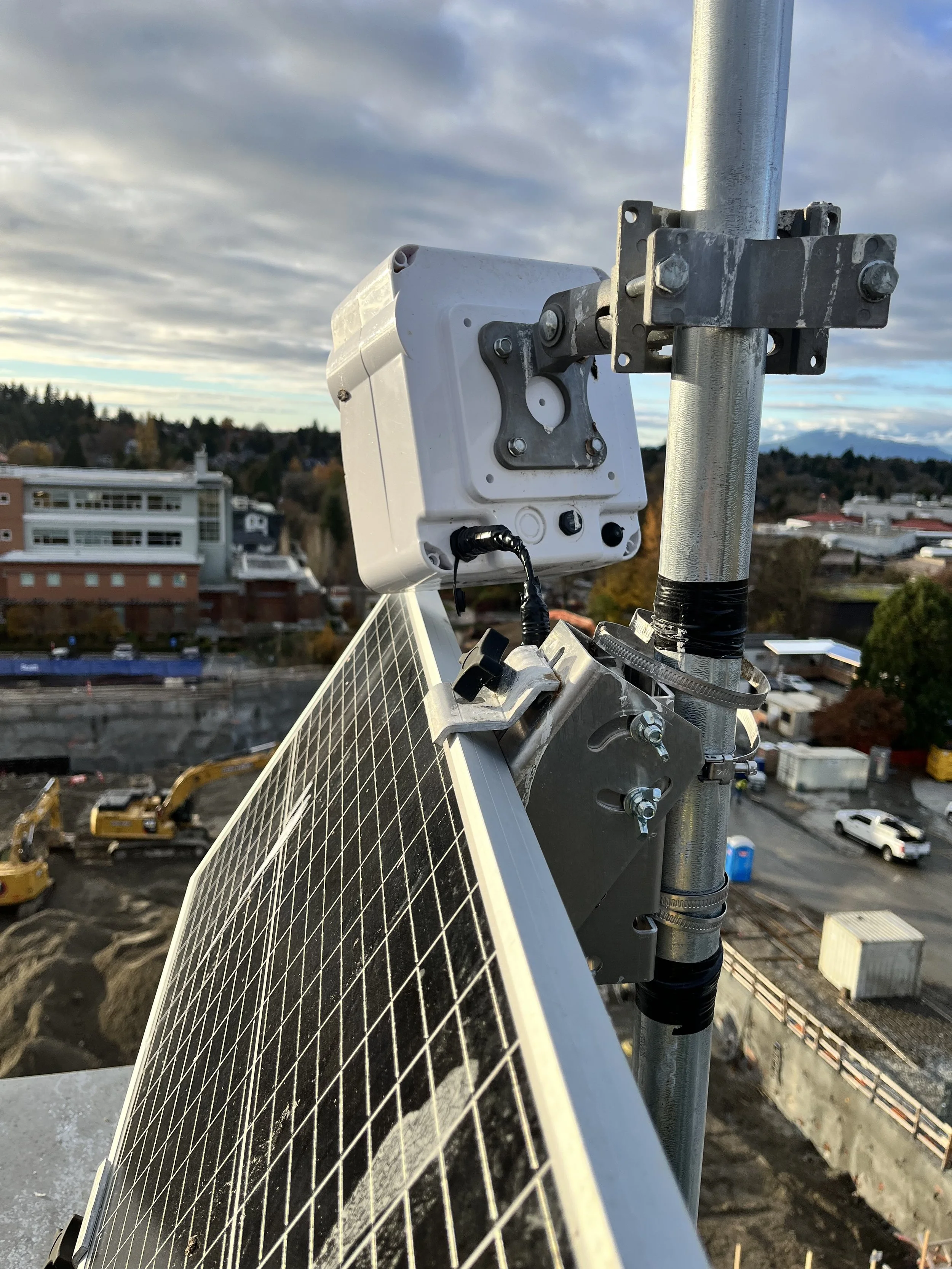 Close-up of a solar panel mounted on a rooftop with construction site and buildings in background.