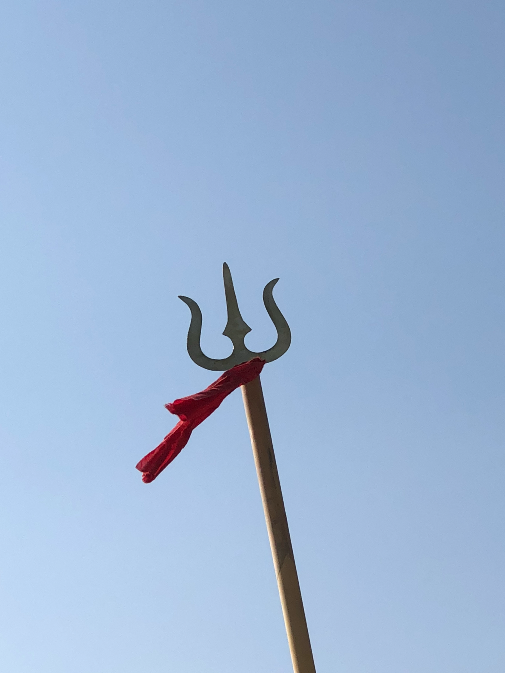 A small metal trident attached to a white stick, with red and black paint, against a clear blue sky.